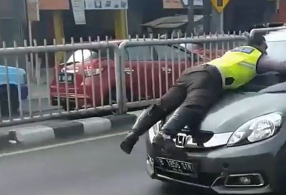 Bripka Eka Setiawan, anggota Unit Lantas Polsek Pasar Minggu, terlihat tertelungkup di atas kap mobil warna abu-abu.