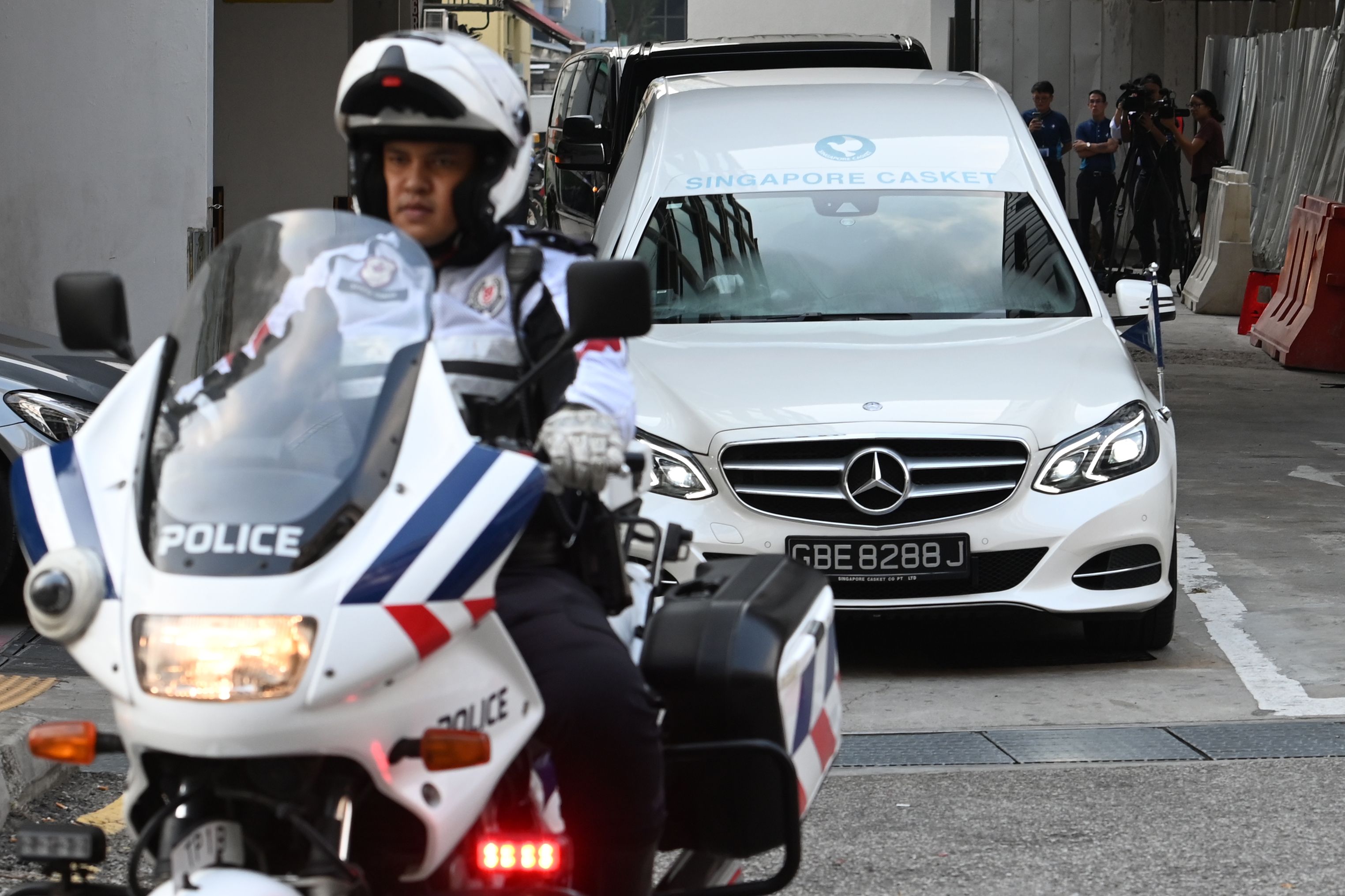 Polisi Singapura mengawal mobil yang mengangkut jenazah Mugabe dari rumah duka menuju bandara untuk dipulangkan ke Zimbabwe.