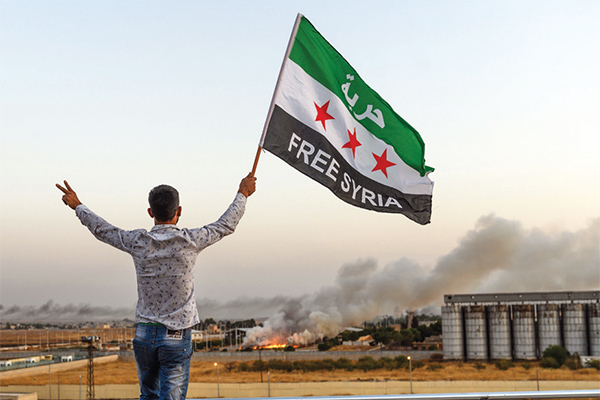 Seorang pria mengibarkan bendera oposisi Suriah bertuliskan ‘Free Syria’ saat pasukan Turki berhasil merebut Kota Tal Talyyad