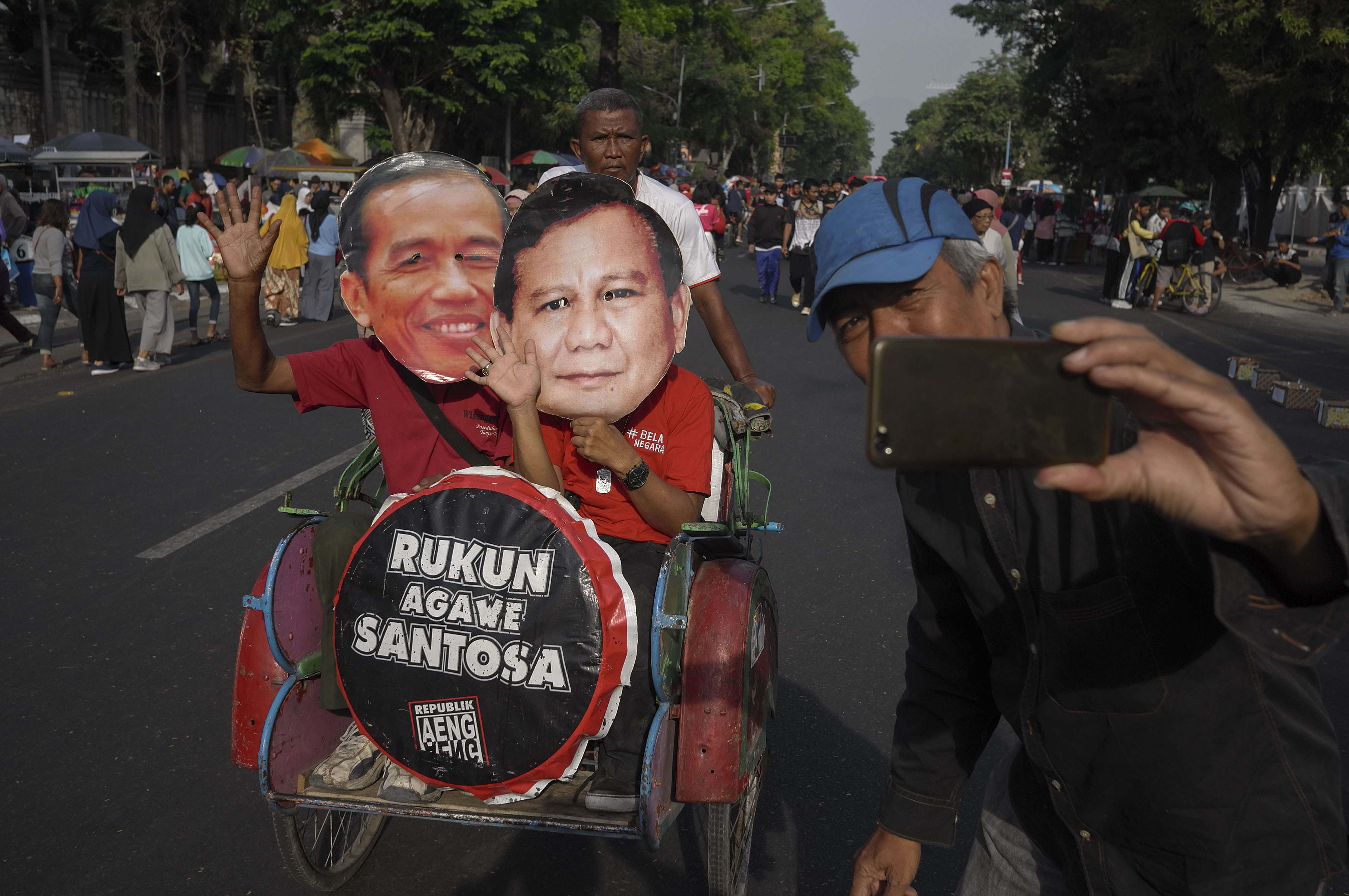 Warga memakai topeng bergambar peserta Pilpres 2019, Joko Widodo (kiri) dan Prabowo Subianto (kanan) saat aksi Rukun Agawe Santoso.
