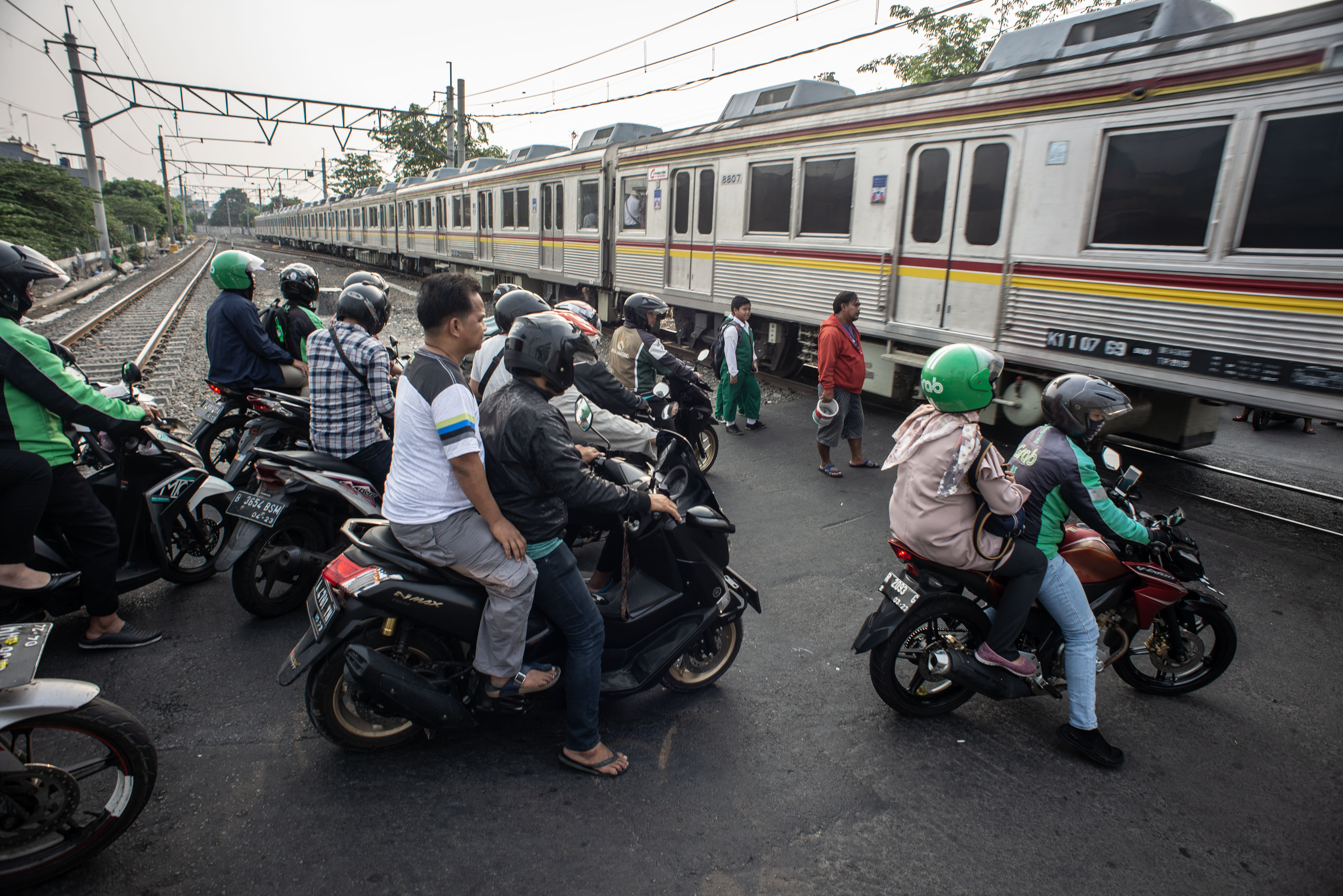 : Pengendara sepeda motor menghentikan kendaraannya saat KRL melintas di perlintasan kereta api tanpa palang pintu di Jakarta.
