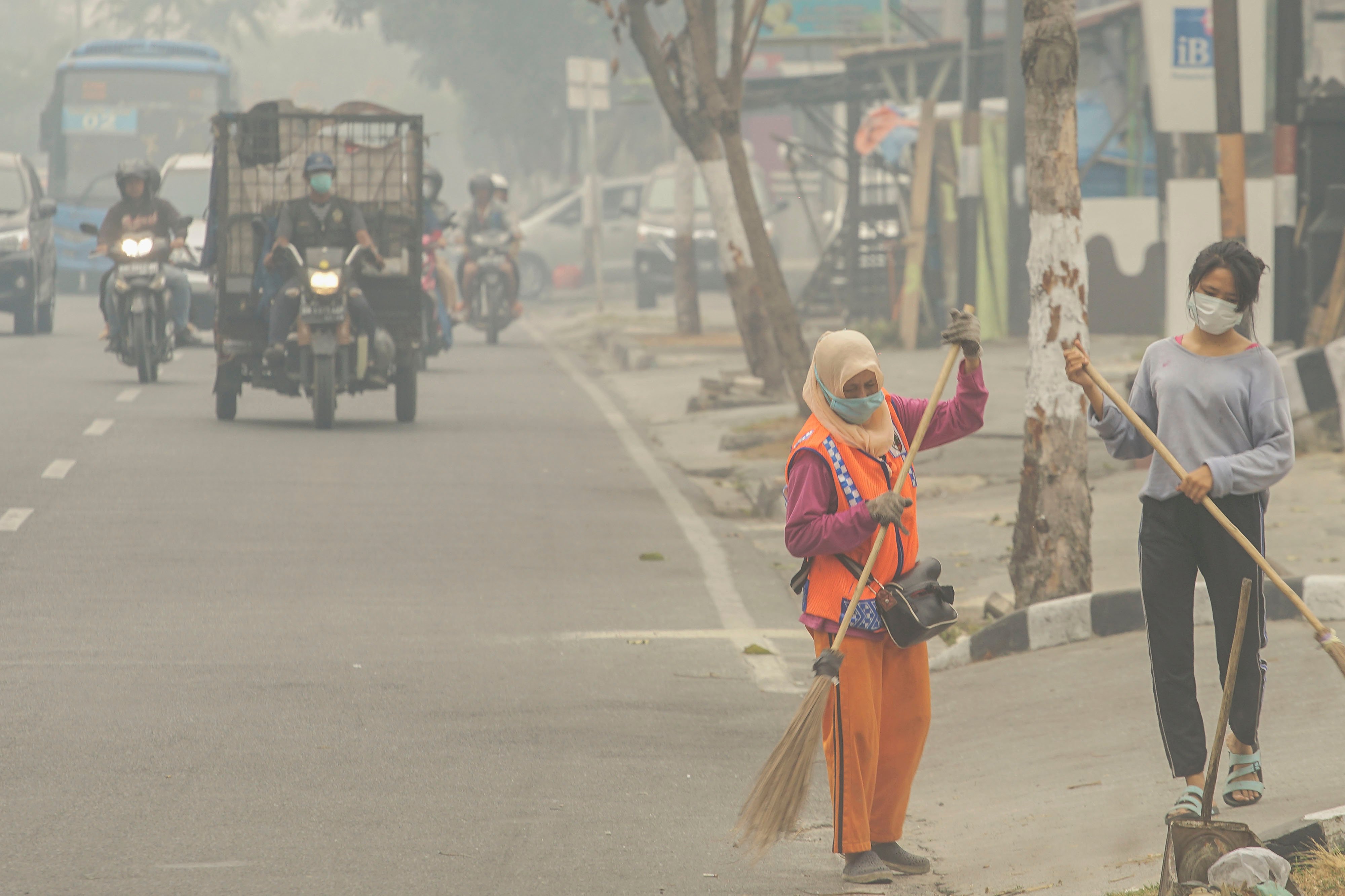 Petugas Kebersihan mengenakan masker ketika menyapu jalan saat kabut asap di Kota Pekanbaru, Riau