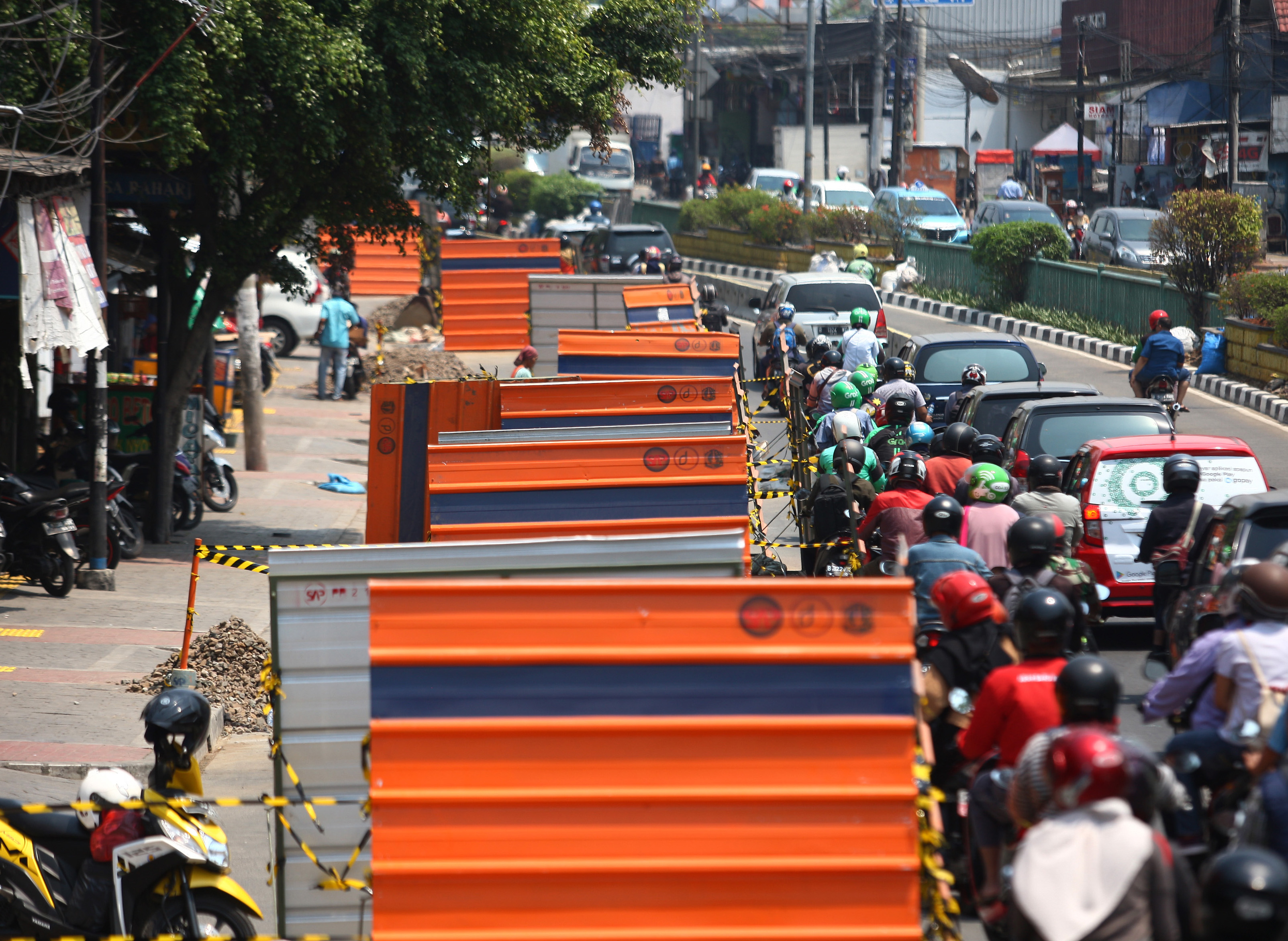  Pengendara bermotor melintas di samping proyek revitalisasi saluran air dan trotoar di kawasan Jalan Otto Iskandardinata, Jakarta