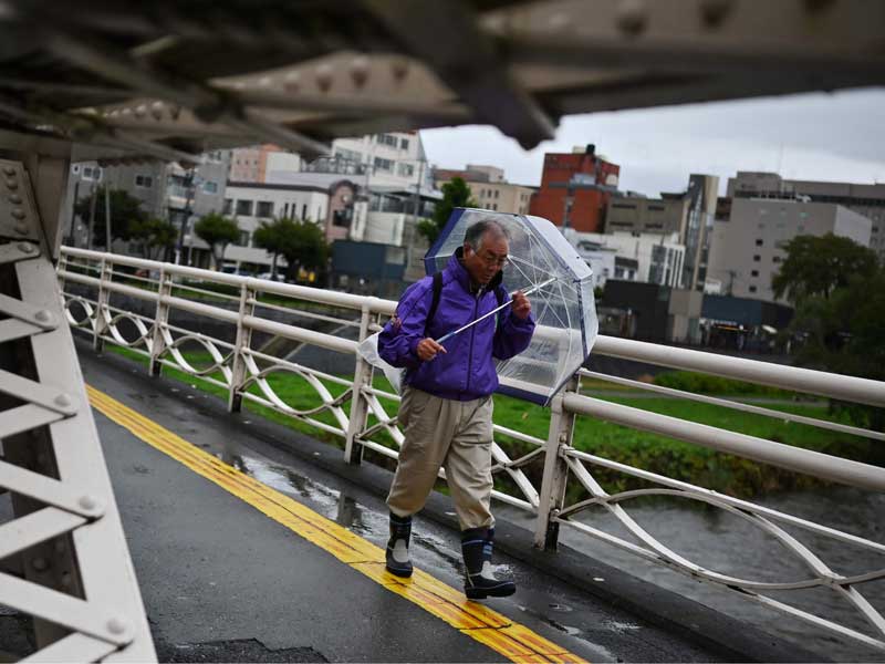 Seorng pejalan kaki berjalan di tengah badai Topan Hagibis di Jepang yang membuat kualifikasi F1 di Sirkuit Suzuka di undur.