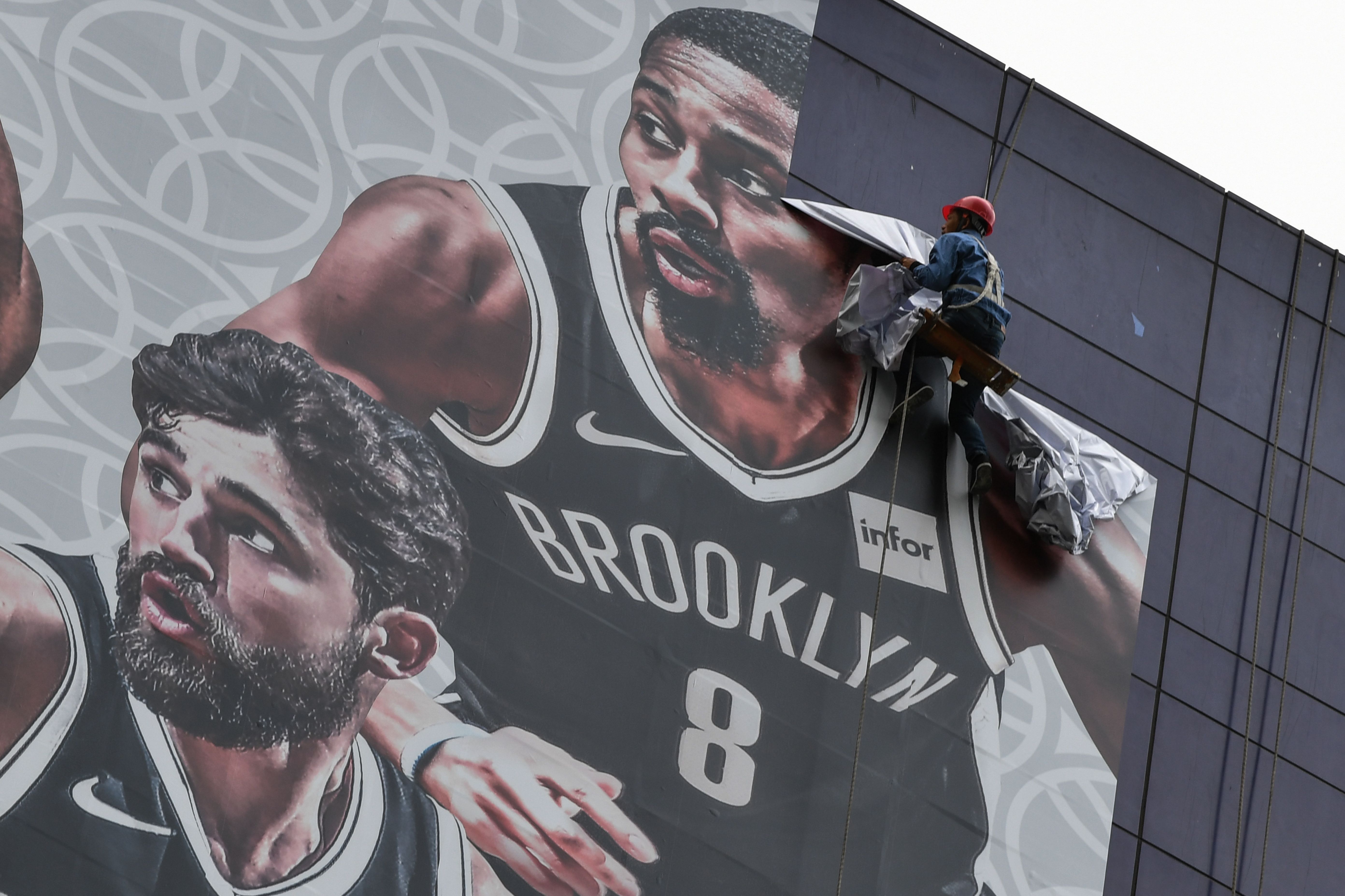 Seorang pekerja mencopot banner promosi laga pramusim antara Brooklyn Nets dan Los Angeles Lakers dari sebuah bangunan di Shanghai, Tiongkok