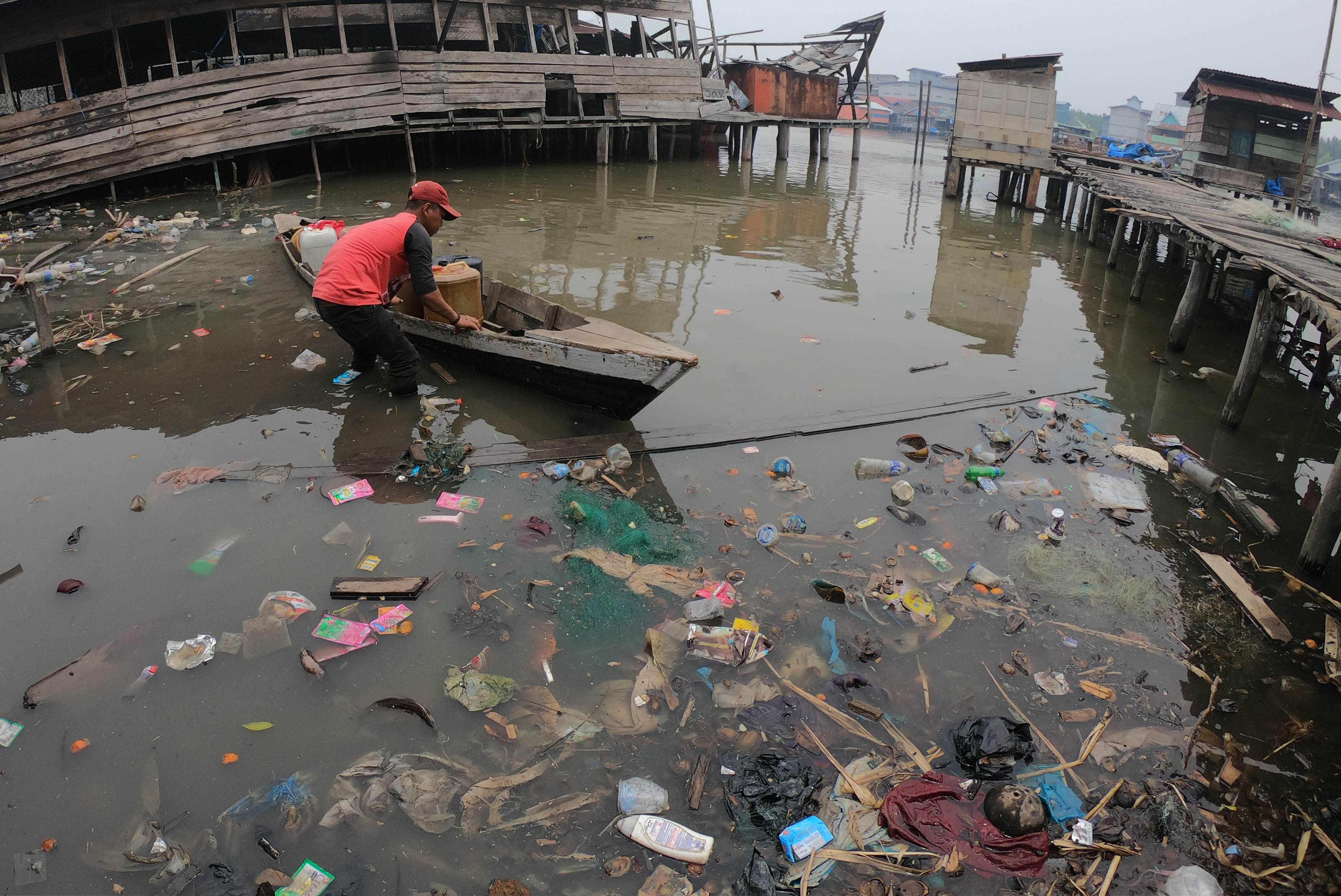 Warga mendorong sampannya keluar dari muara Sungai Air Hitam Laut yang tercemar sampah plastik di Tanjungjabung Timur, Jambi.