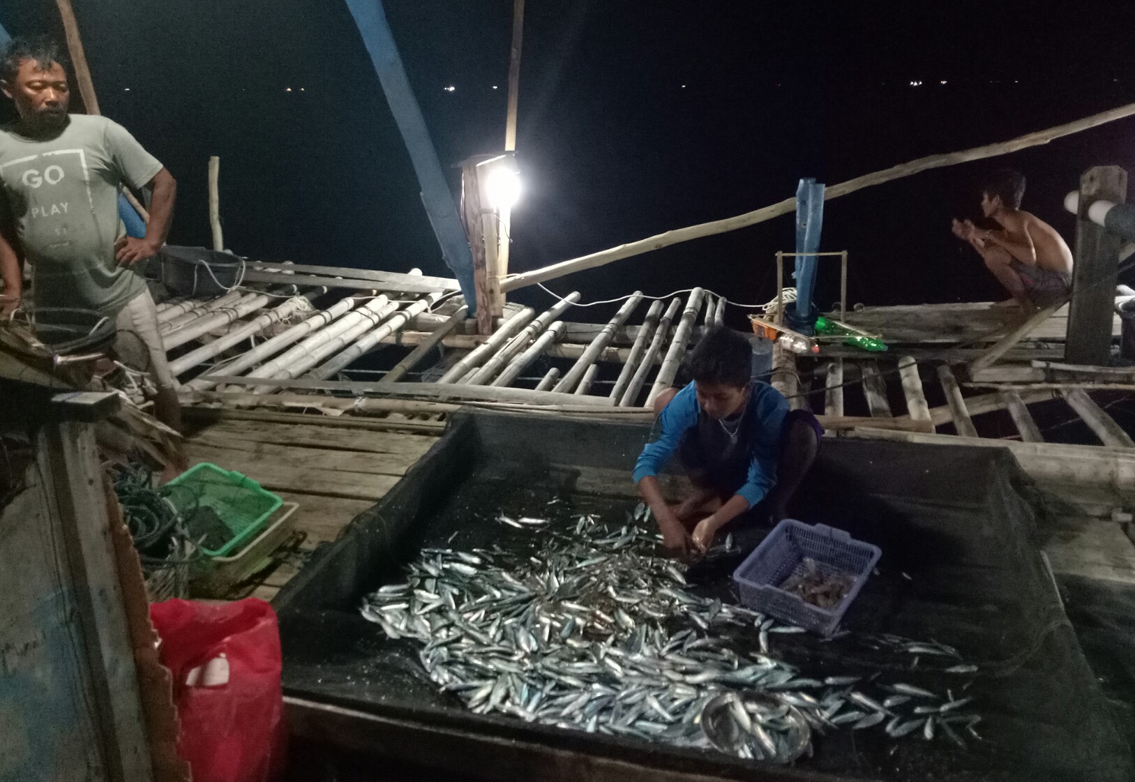 Para nelayan memanen ikan hasil dari memancing dengan menggunakan lampu pijar.