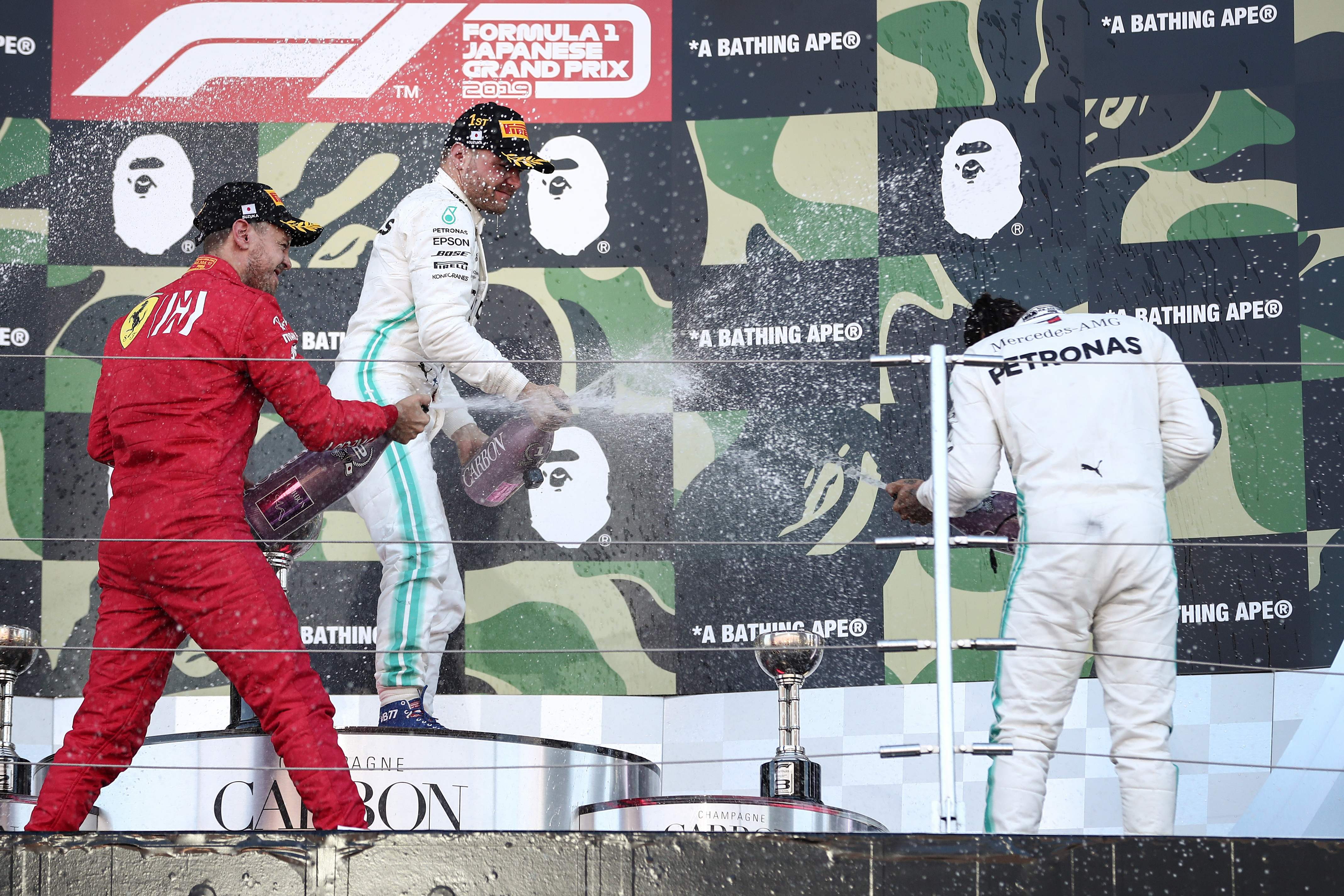 Pembalap Mercedes Valtteri Bottas (tengah) menyemprotkan sampanye ke arah rekan setimnya, Lewis Hamilton (kanan), seusai GP Jepang berakhir.