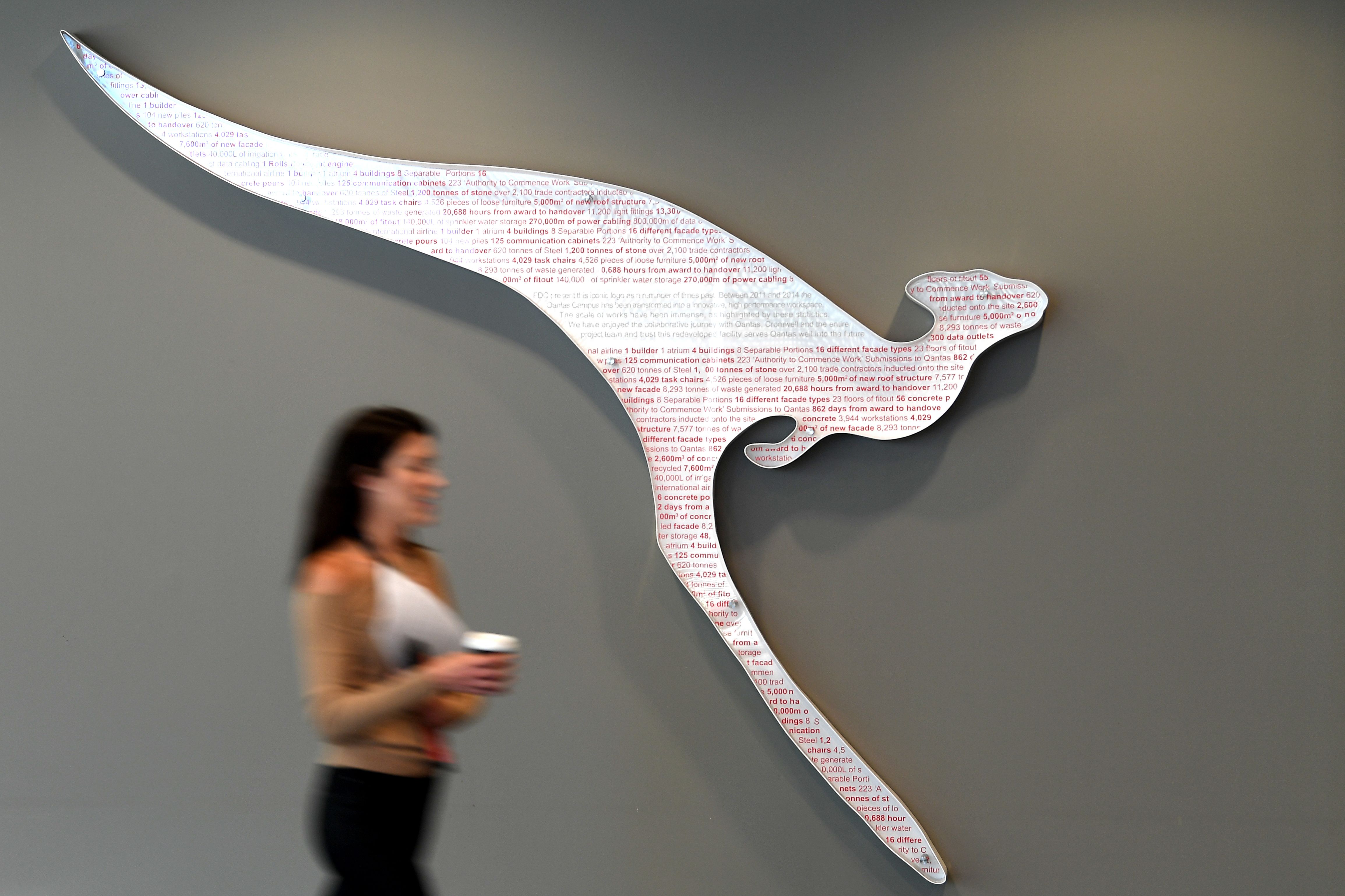 Seorang perempuan berjalan di depan logo maskapai penerbangan Australia Qantas