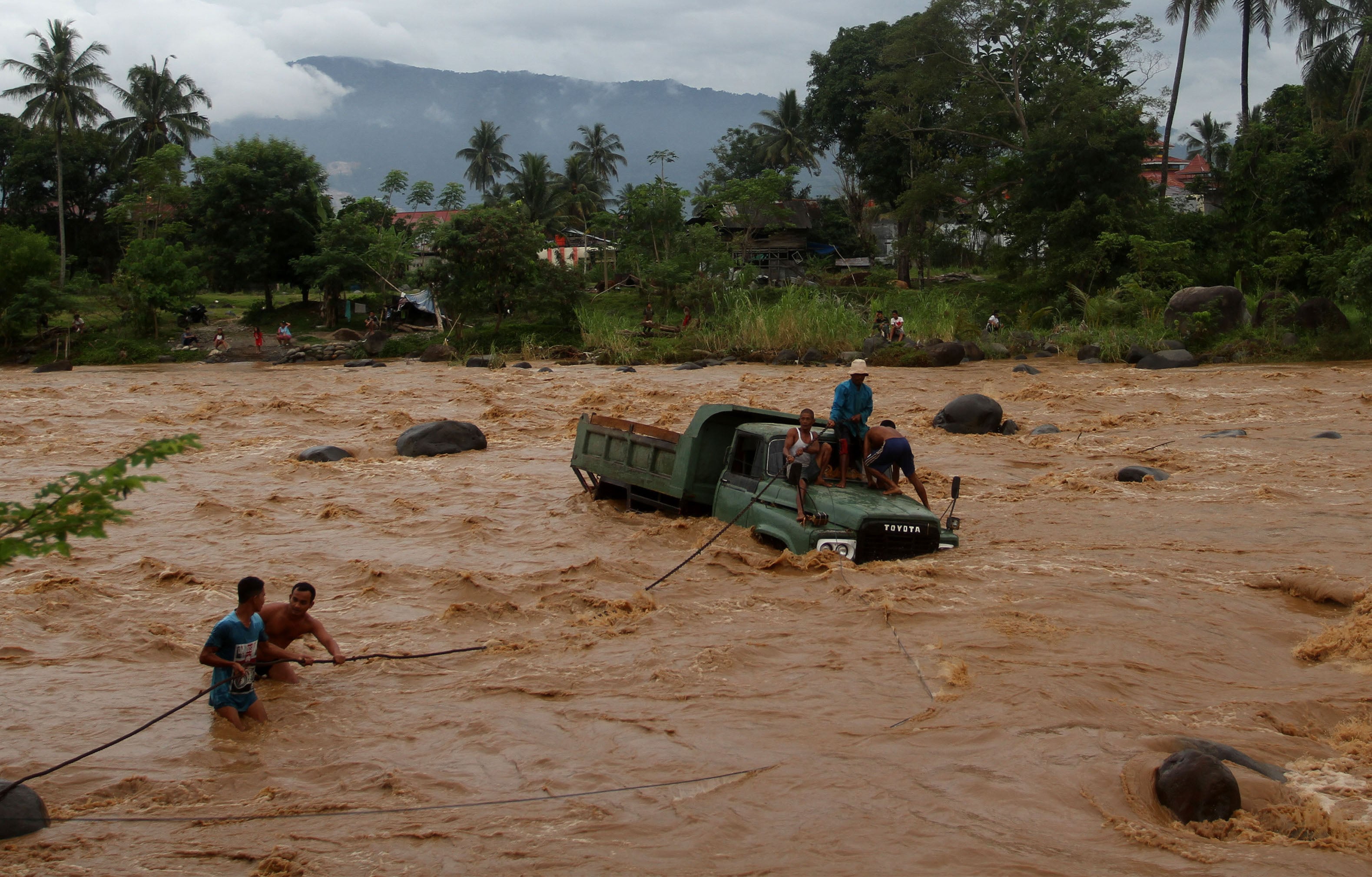Warga berusaha menarik mobil truk pengangkut batu yang berada di tengah sungai Batang Kuranji akibat terseret banjir di Kecamatan Pauh,
