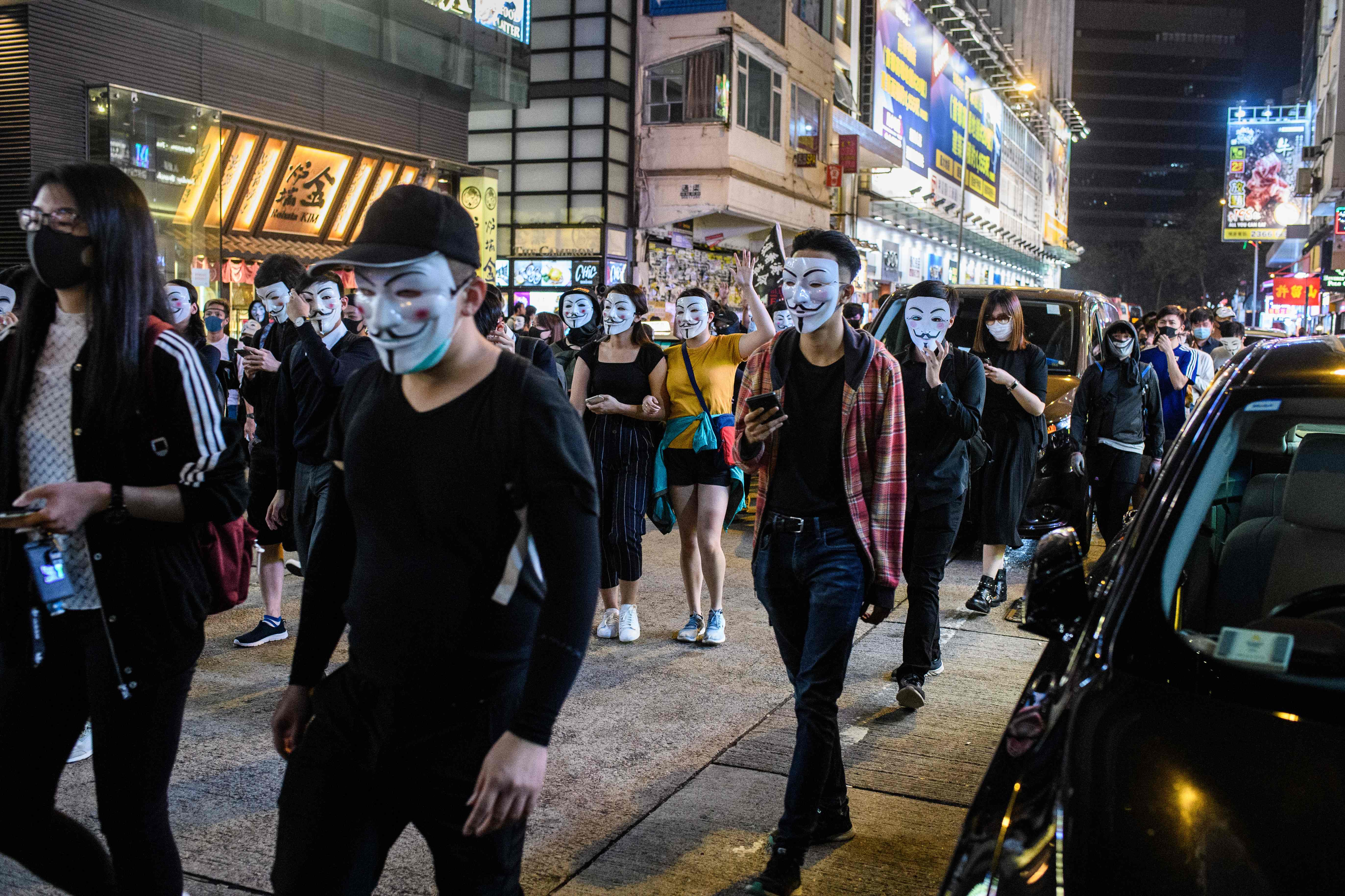 Para demonstran mengenakan topeng Guy Fawkes berjalan distrik Kowloon,  Hong Kong. 