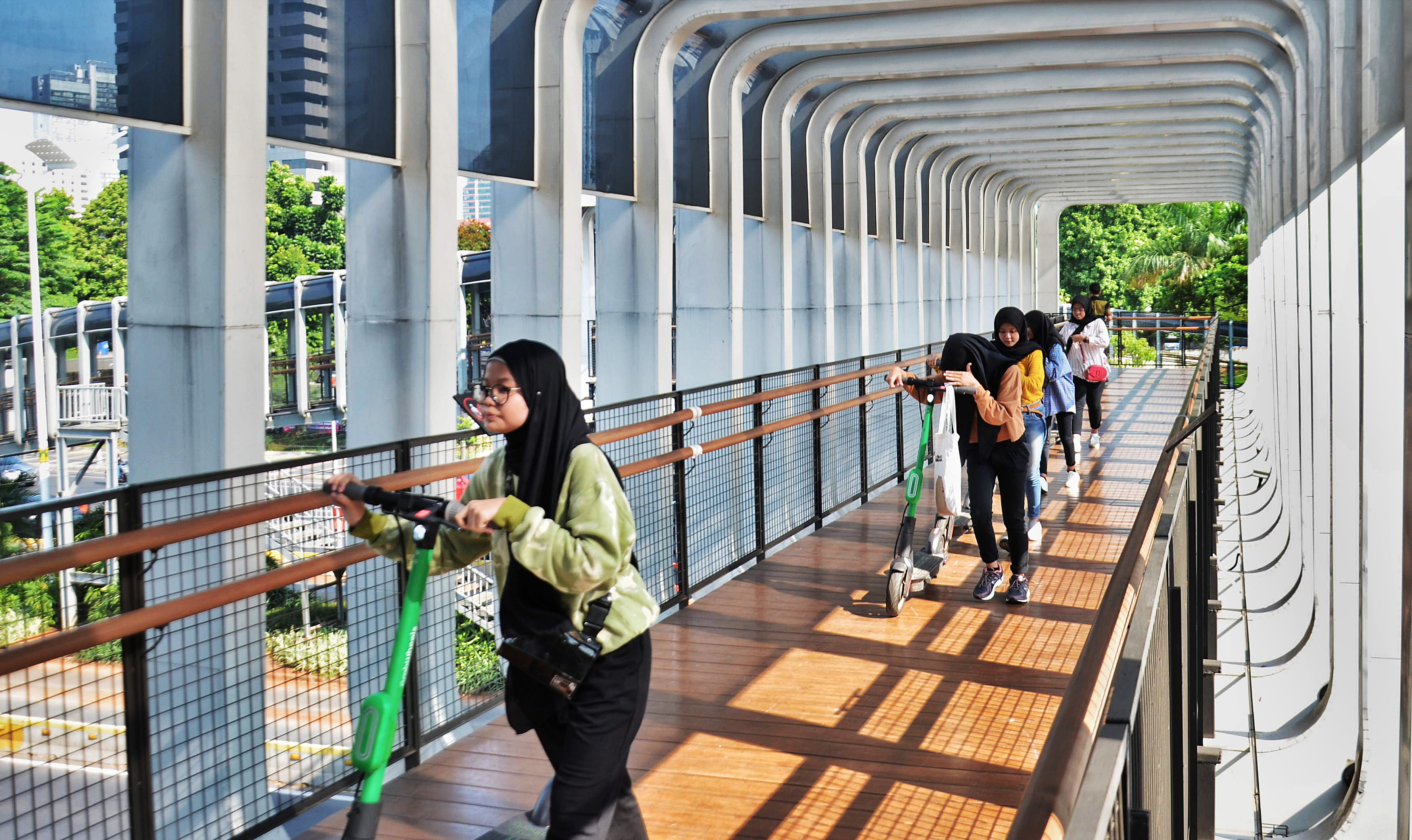 Warga melintas di atas JPO Senayan sembari membawa sekuter listrik, Sabtu (16/11)