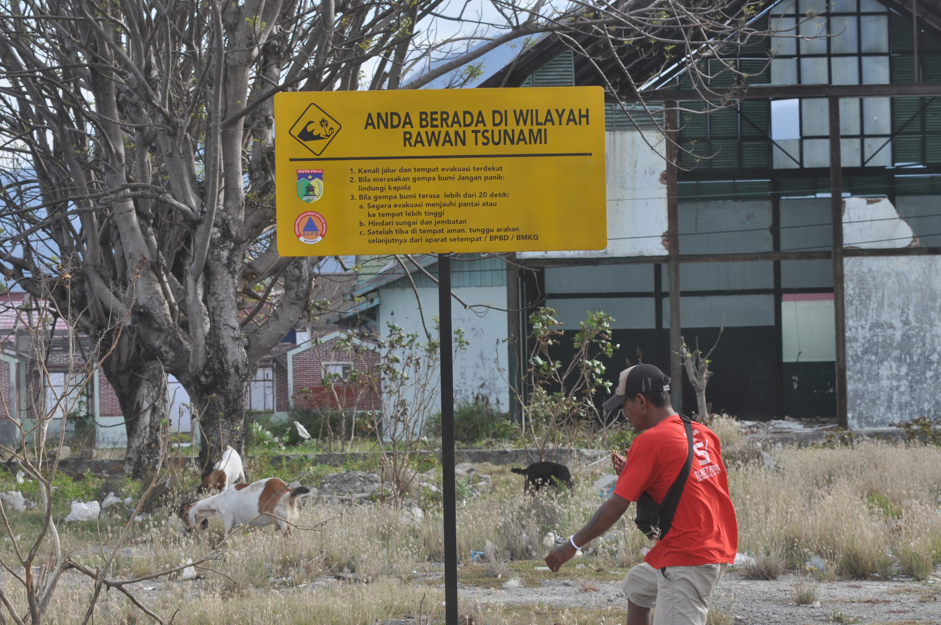 Warga berada disekitar rambu berisikan pemberitahuan daerah rawan tsunami serta langkah yang perlu dilakukan bila terjadi gempa dan tsunami