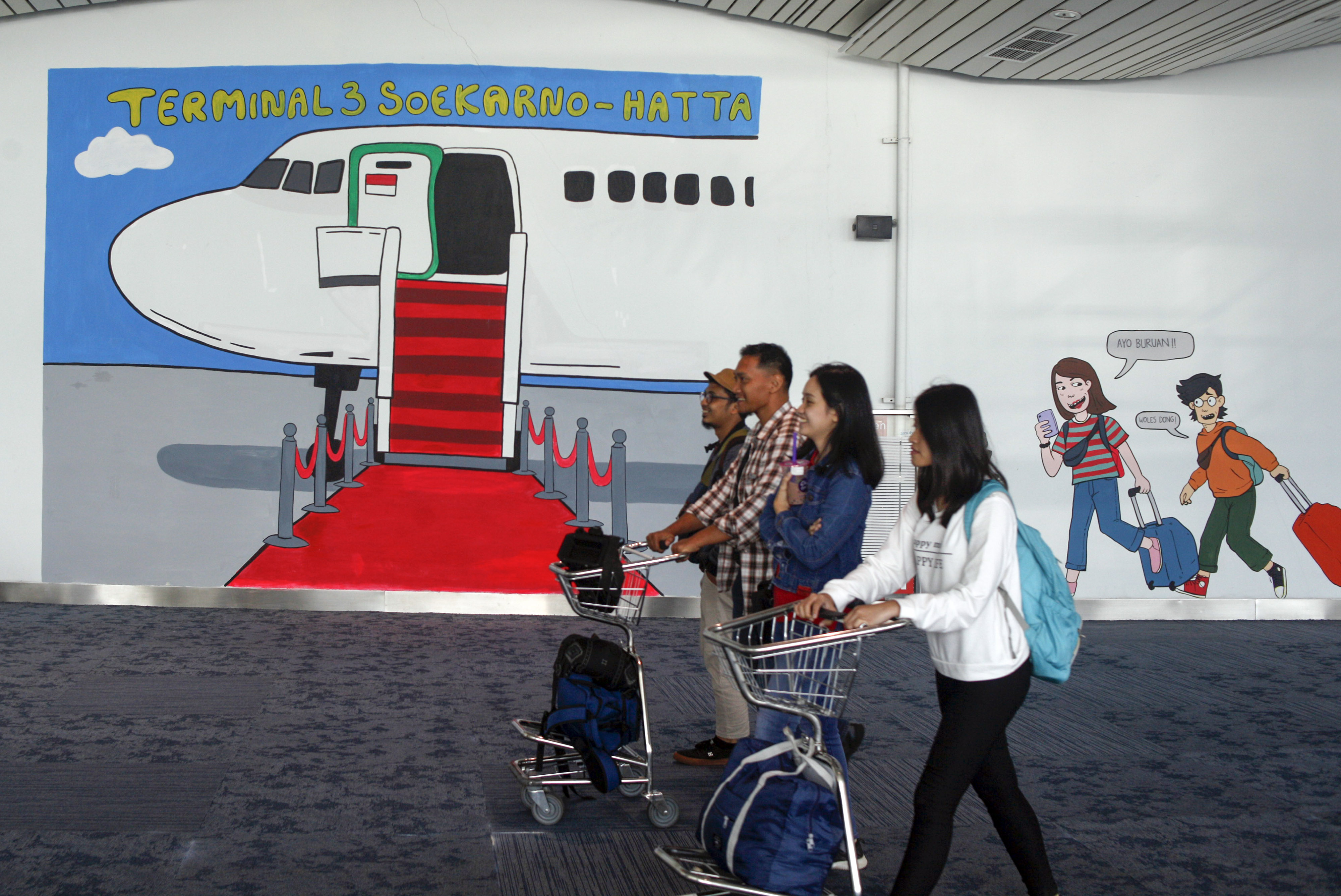  Sejumlah penumpang pesawat melintas di samping mural di terminal 3, Bandara Soekarno Hatta, Tangerang, Banten.