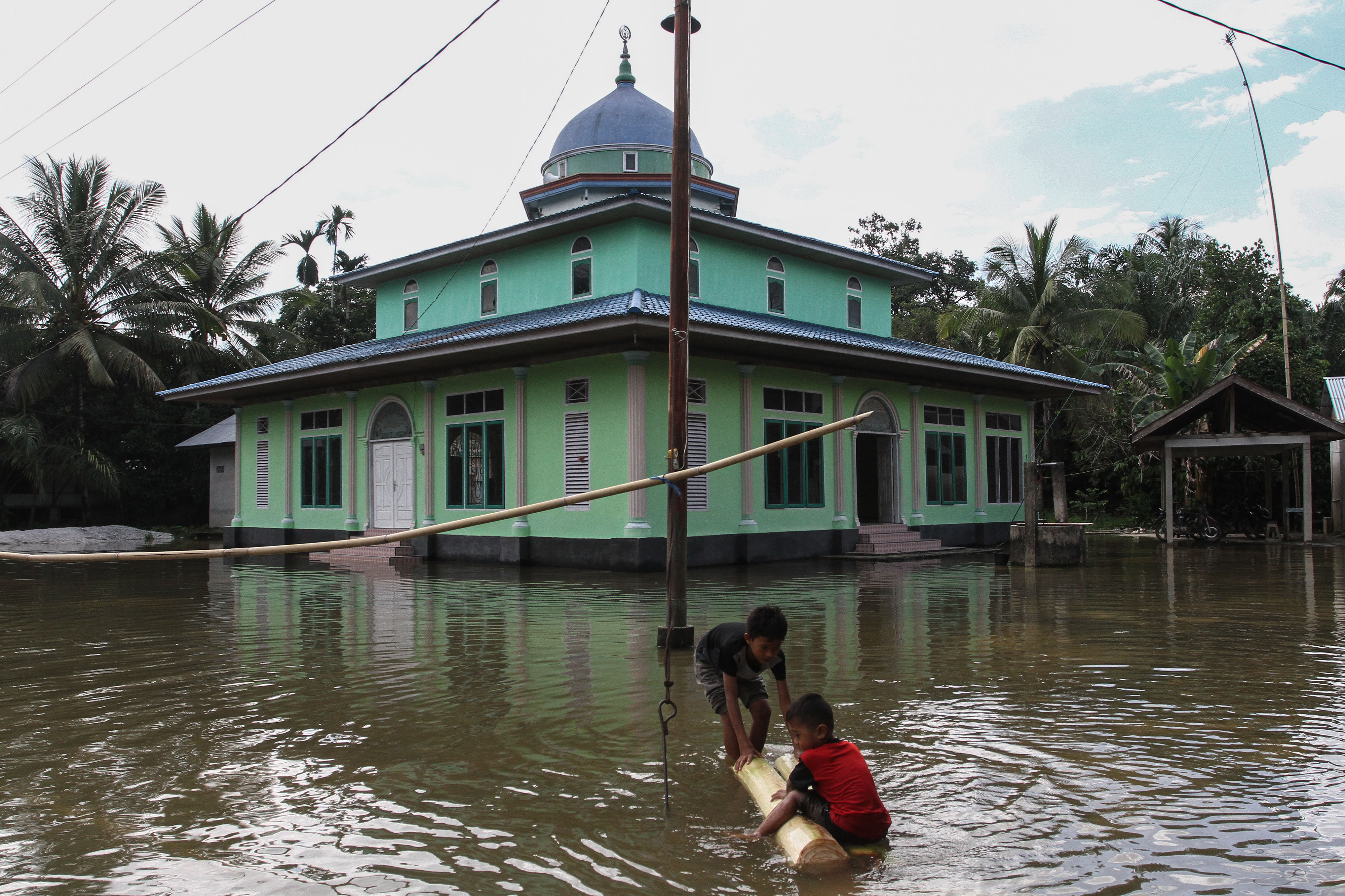Dua anak bermain di halaman masjid yang terendam banjir akibat luapan Sungai Kampar di Desa Rumbio Jaya, Riau, Jumat (13/12).