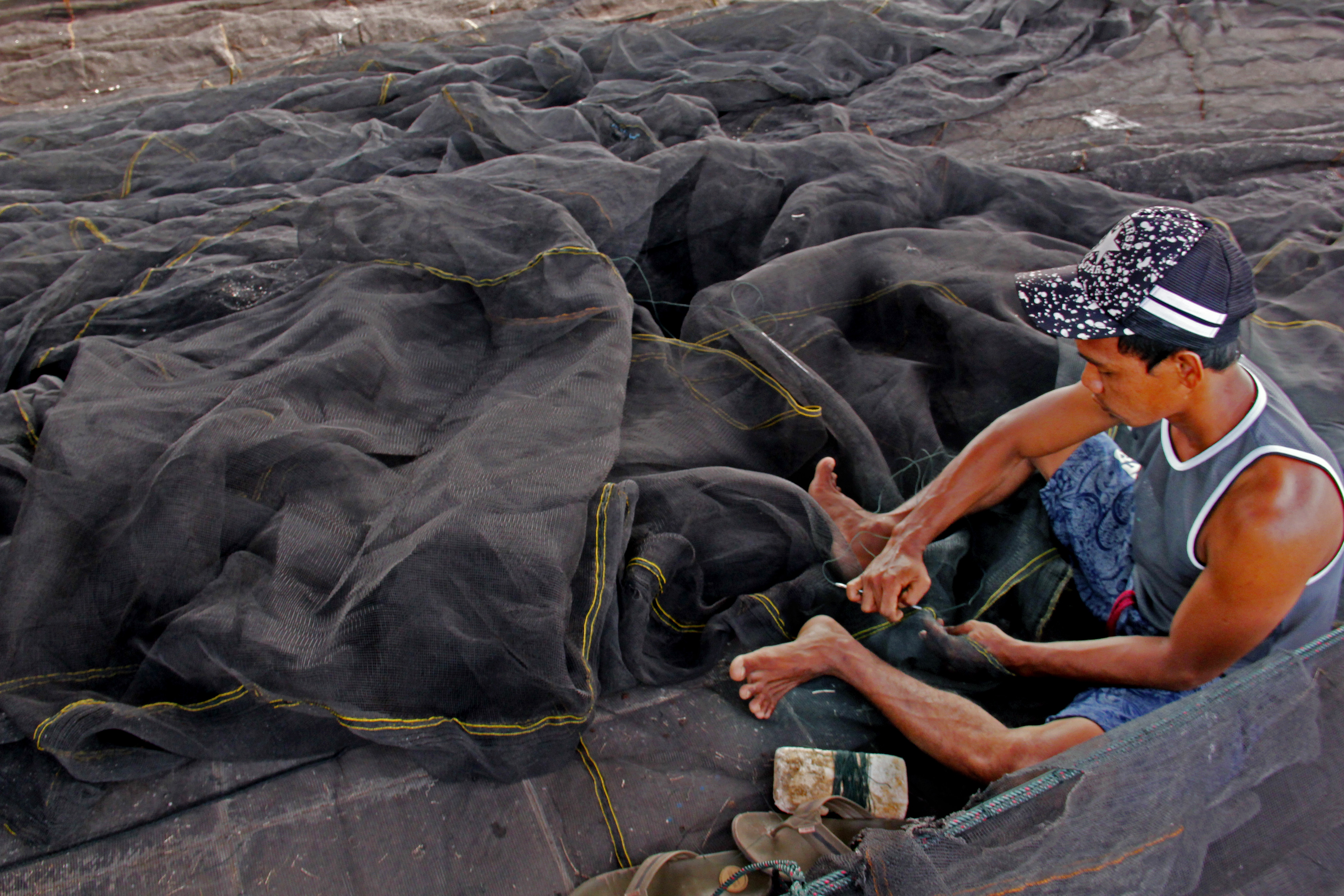 Nelayan memperbaiki jaring ikan jenis waring di Pelabuhan Perikanan Bojonegara, Serang, Banten.