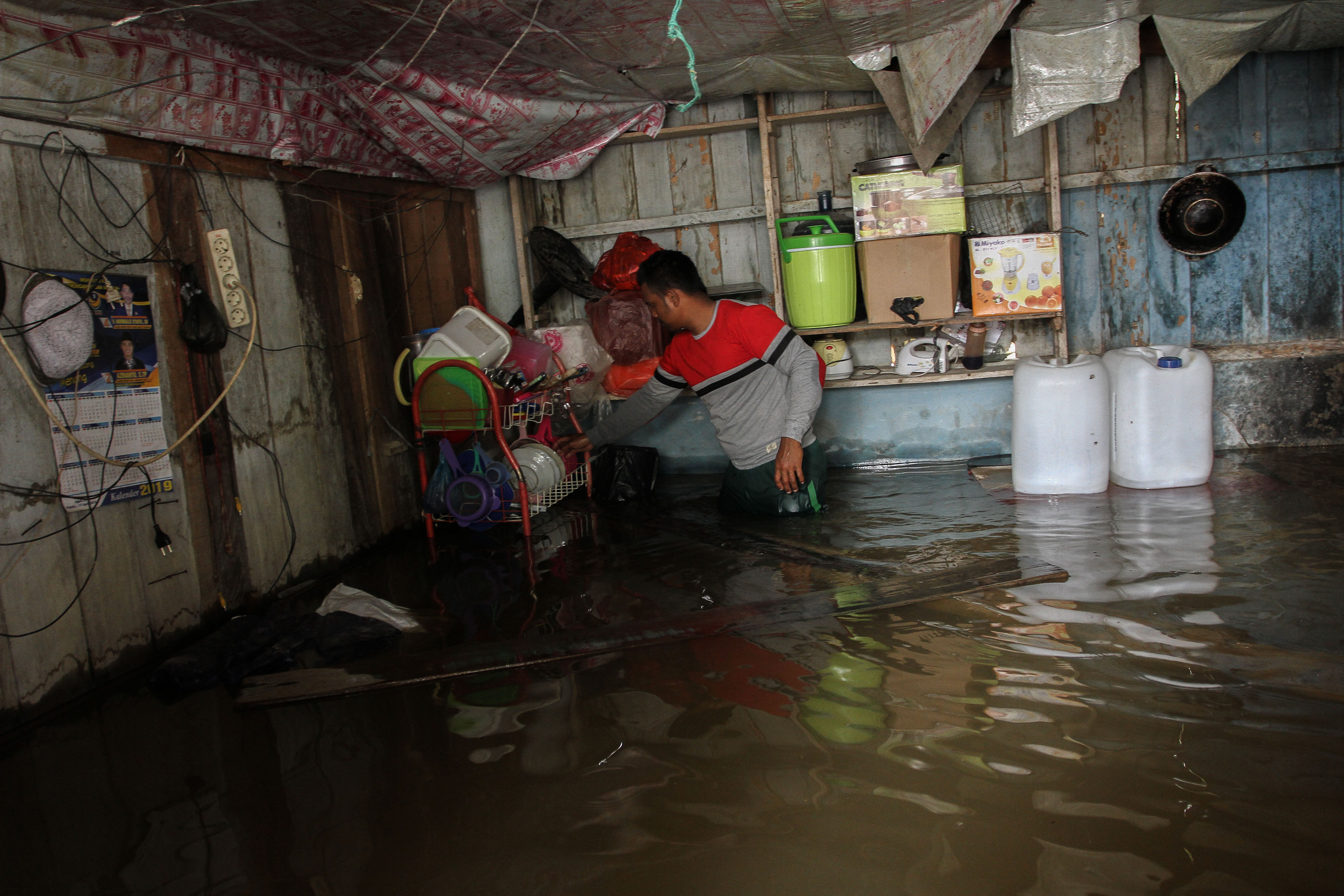 Pemilik warung kopi memindahkan peralatan dapur yang terendam banjir ke tempat yang lebih tinggi ketika terjadi banjir luapan Sungai Kampar.