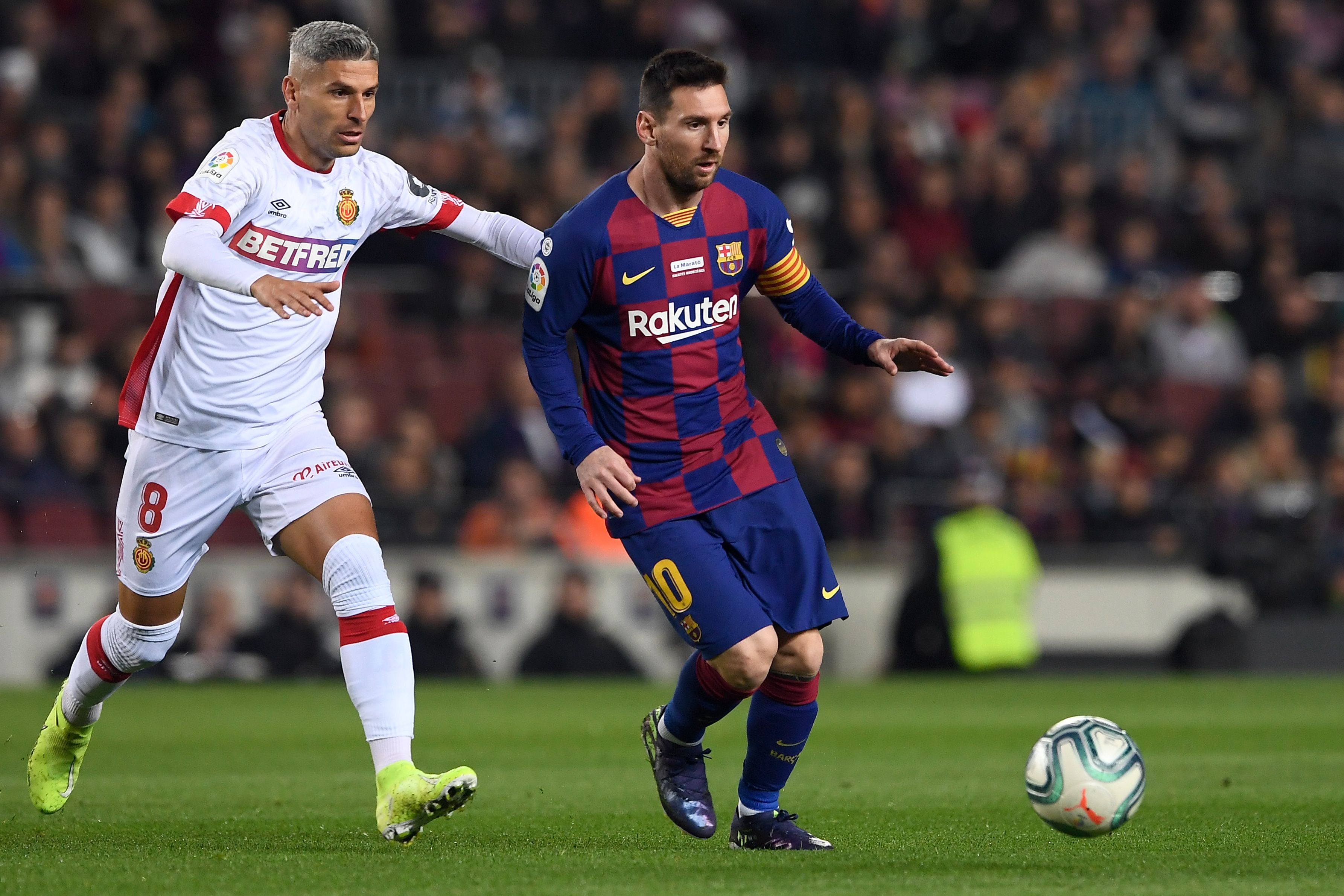 Pemain Real Mallorca, Salva Sevilla (kiri) berebut bola dengan pemain Barcelona, Lionel Messi dalam Liga Spanyol, Minggu (8/12/2019)