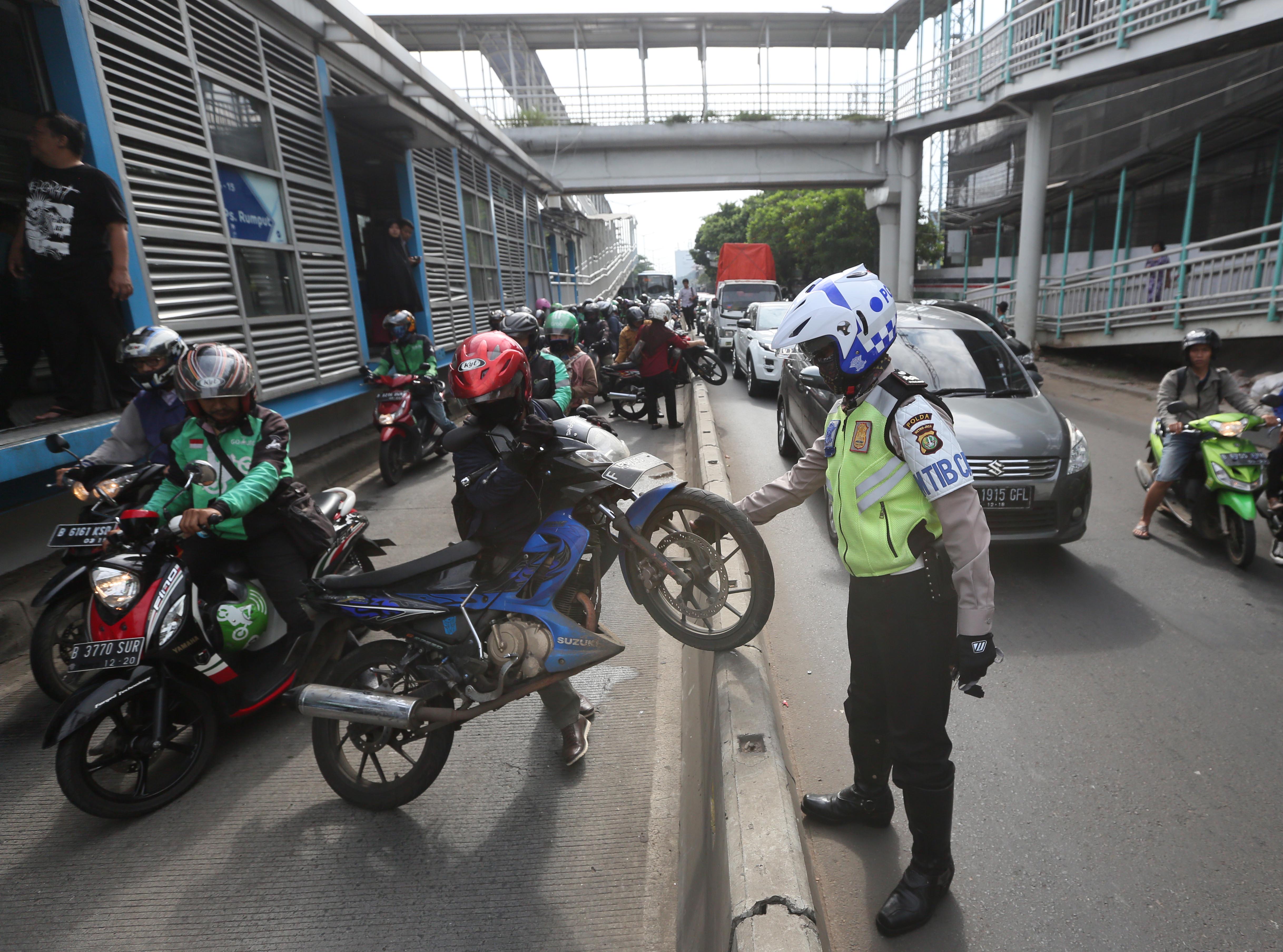 Polisi menjaga pengendara sepeda motor yang berusaha mengangkat motor melewati pembatas jalur setinggi 60 cm