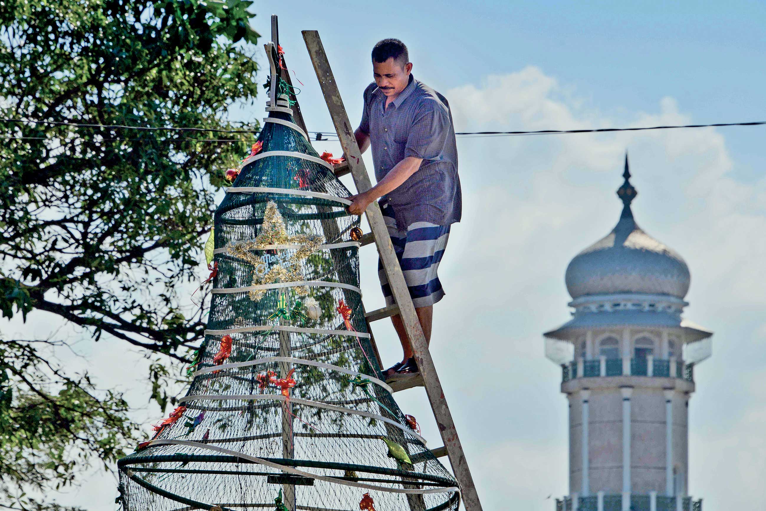 Pekerja memasang hiasan pohon Natal di Gereja Hati Kudus dengan latar belakang menara Masjid Raya Baiturrahman di Banda Aceh, kemarin.
