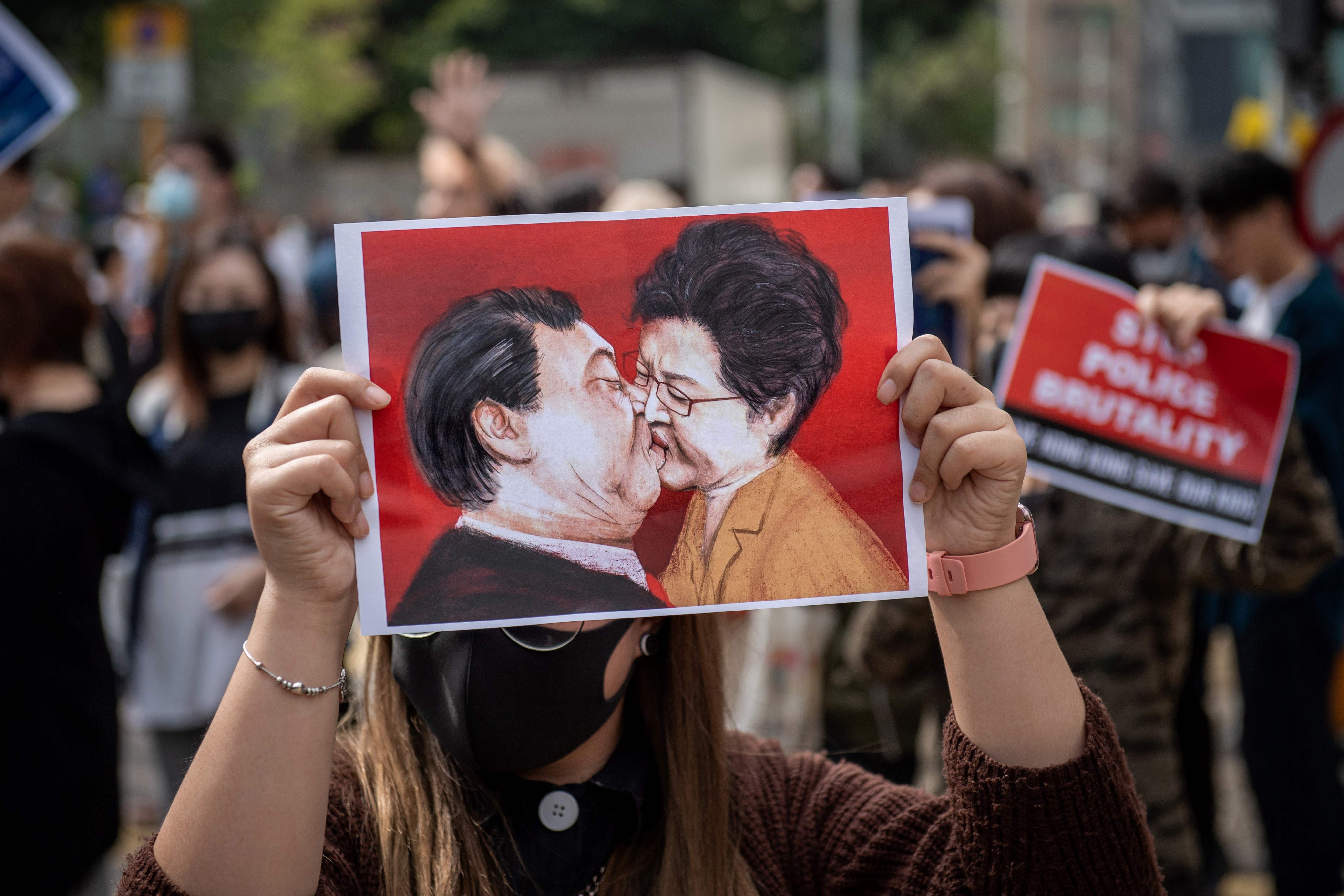 Seorang wanita memegang gambar yang menggambarkan Presiden Cina Xi Jinping (kiri) mencium Kepala Eksekutif Hong Kong Carrie Lam (kanan).
