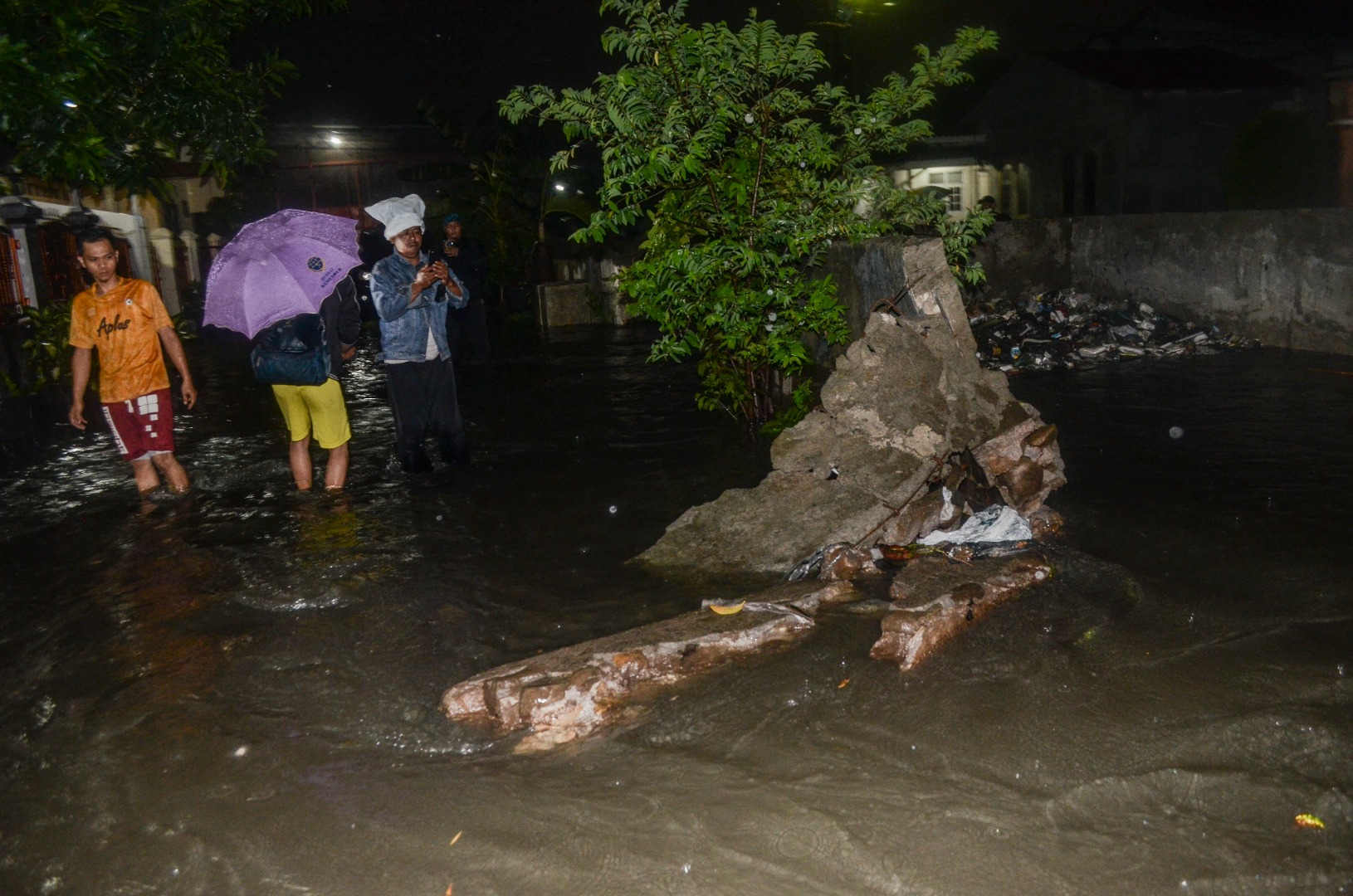 Warga melintasi jalan terendam banjir akibat tanggul jebol di perumahan Cahaya Kemang Permai, Jatibening, Bekasi, Jawa Barat.