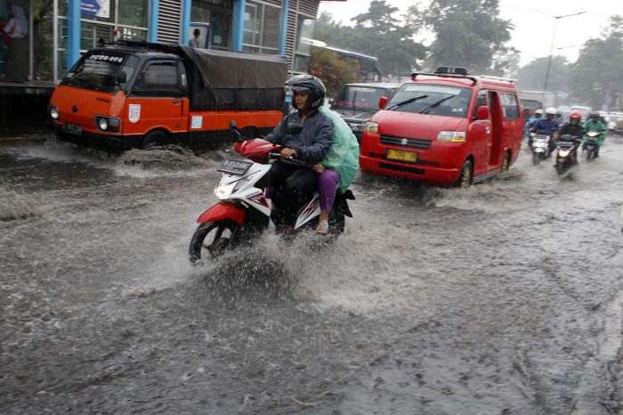 Pengemudi kendaraan bermotor melintasi jalan yang tergenang air