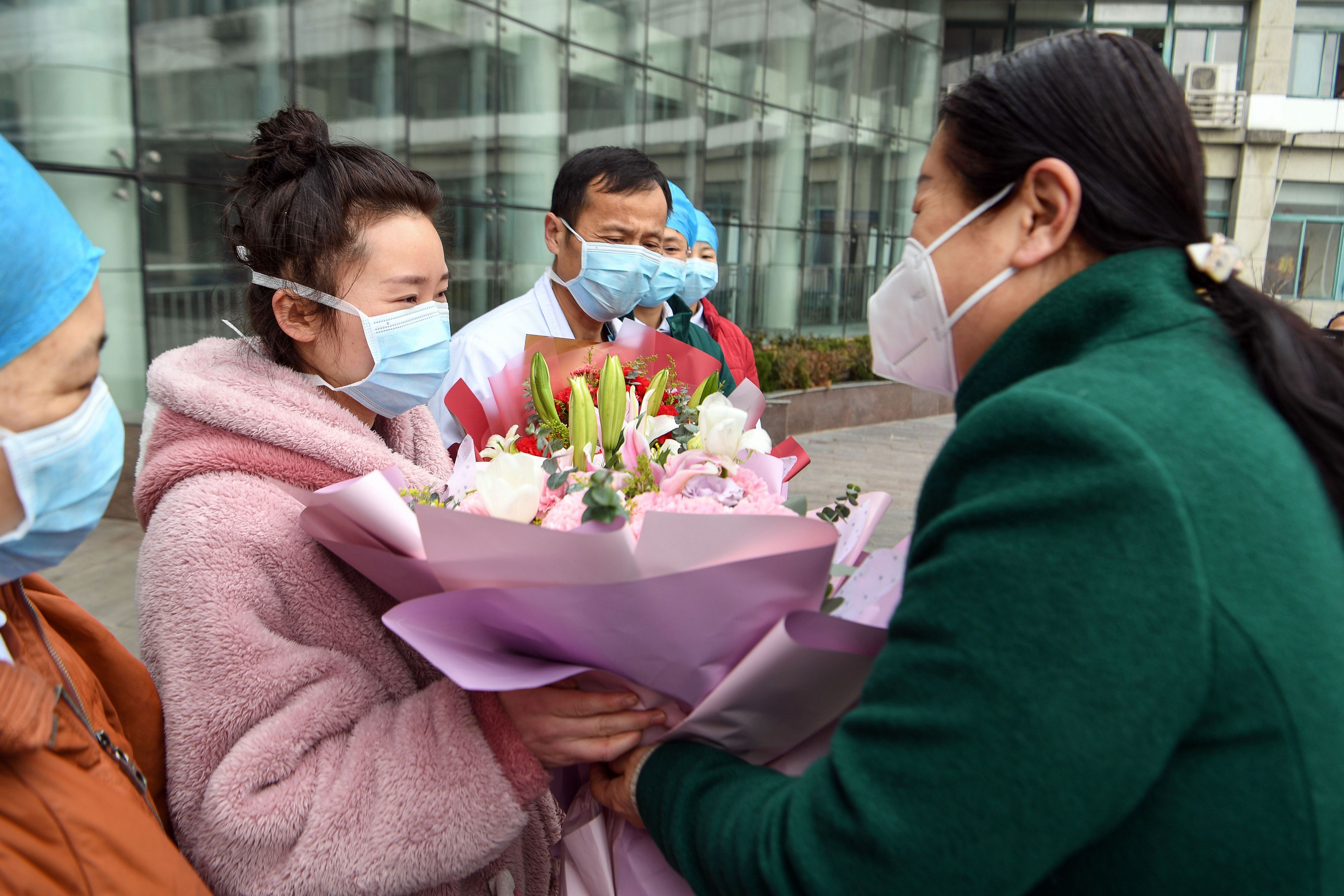 Seorang perempuan yang sembuh dari infeksi virus korona, menerima rangkaian bunga setelah keluar dari rumah sakit di Bozhou, Provinsi Anhui.
