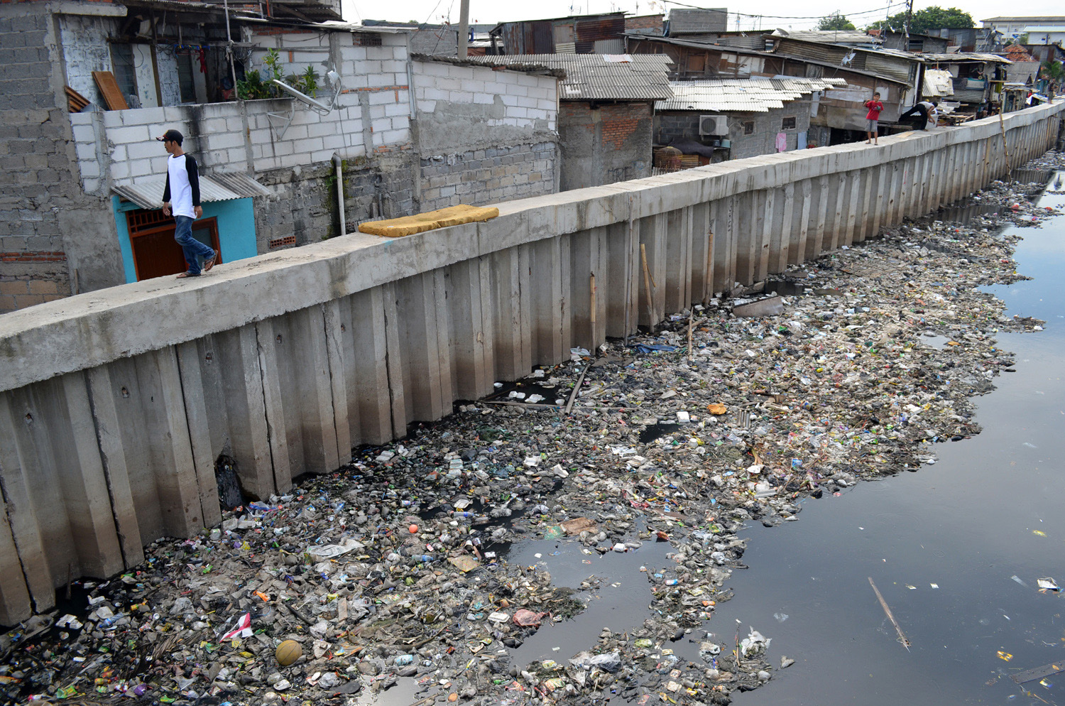 Seorang warga berjalan di tanggul Kali Sekretaris yang berwarna hitam dan dipenuhi sampah di Grogol, Jakarta Barat, 2013