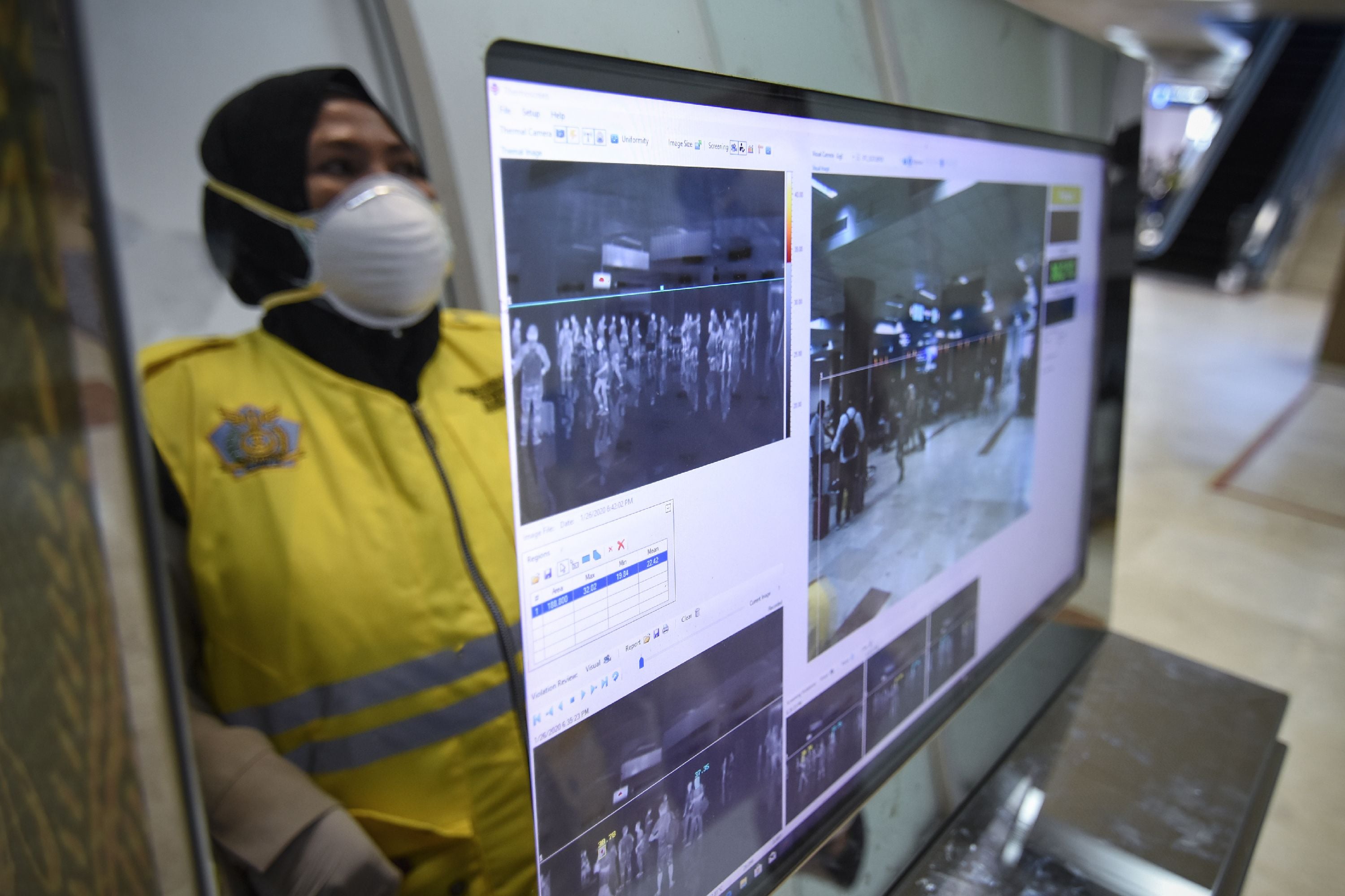 Seorang petugas keamanan berdiri di depan monitor pendeteksi suhu tubuh di Bandara Lombok.