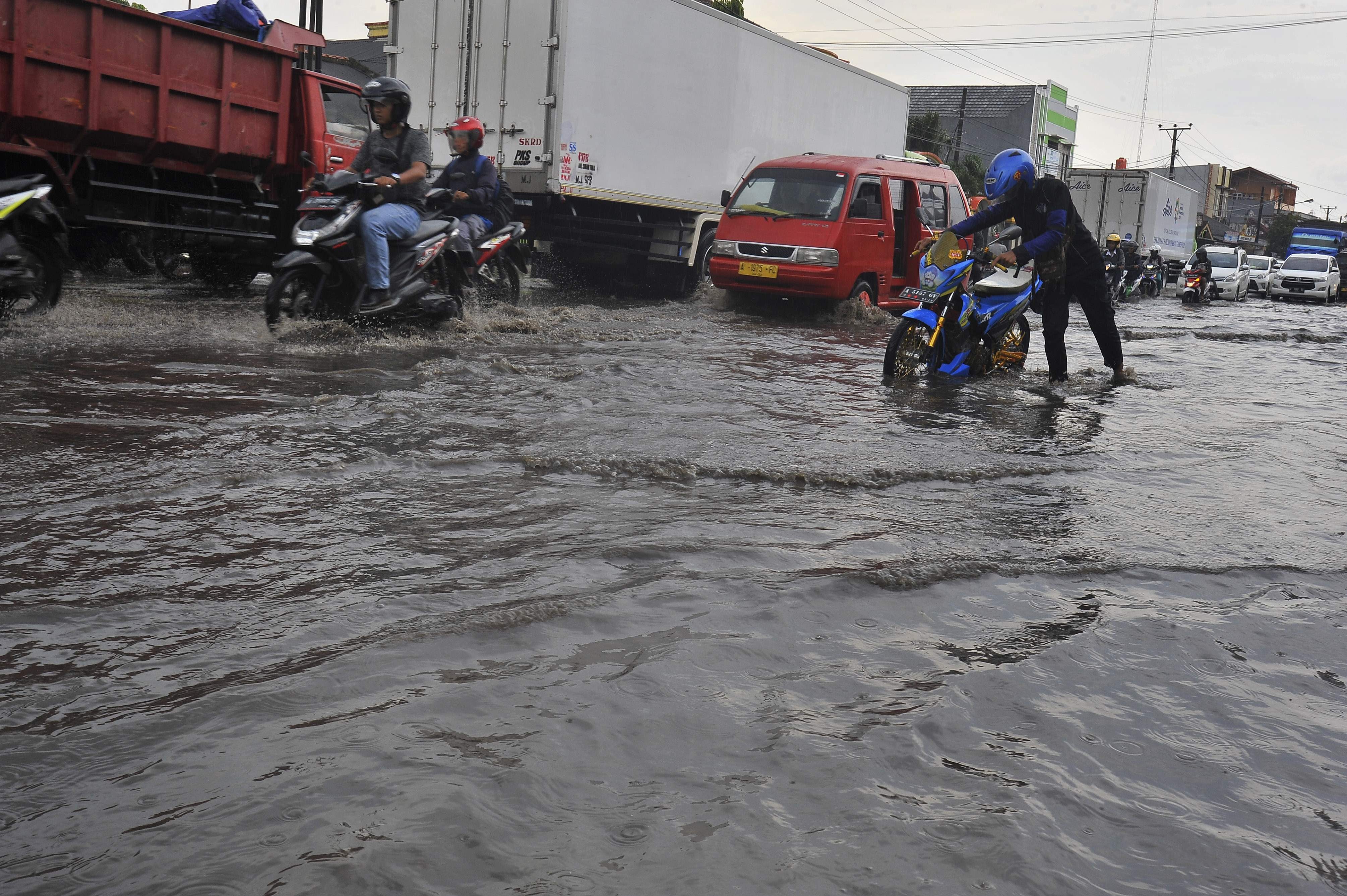 Warga mendorong sepeda motor yang mogok saat melintasi banjir di Jalan Sudirman, Serang, Banten.