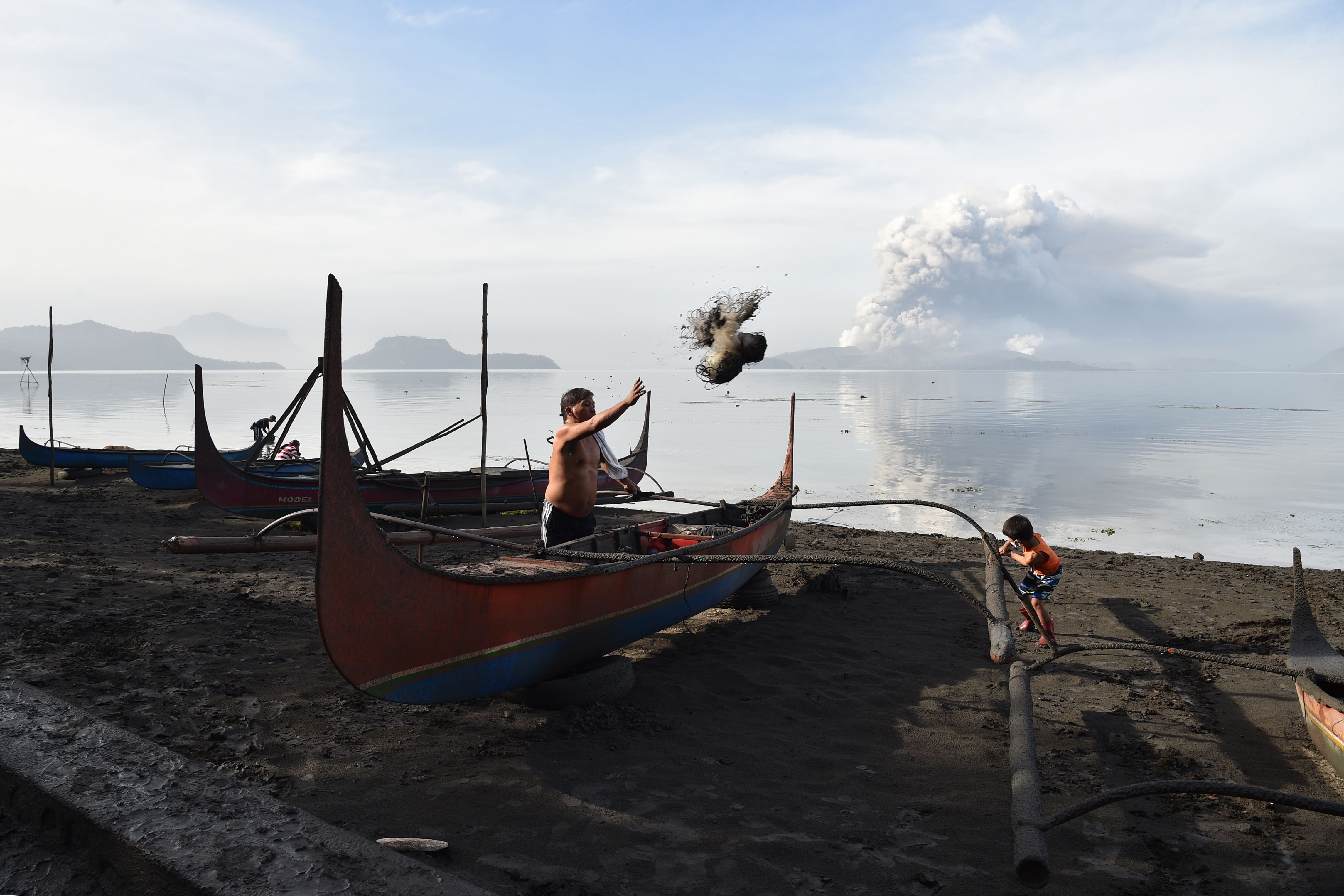 Nelayan membersihkan debu dari kapalnya akibat letusan Gunung Taal
