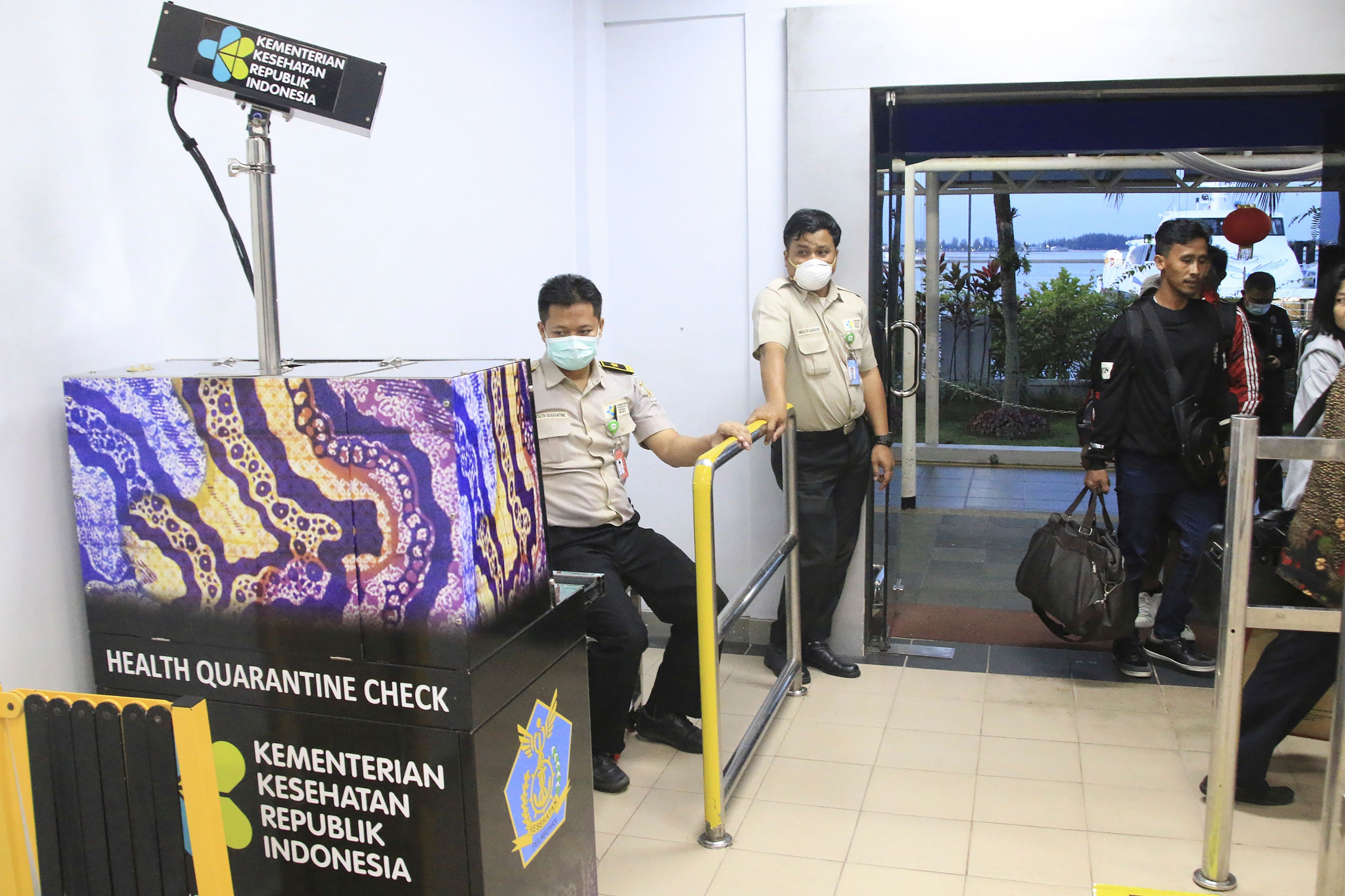 Petugas mengenakan masker memeriksa layar monitor yang memeriksa suhu tubuh penumpang yang tiba di Bandara Internasional Batam