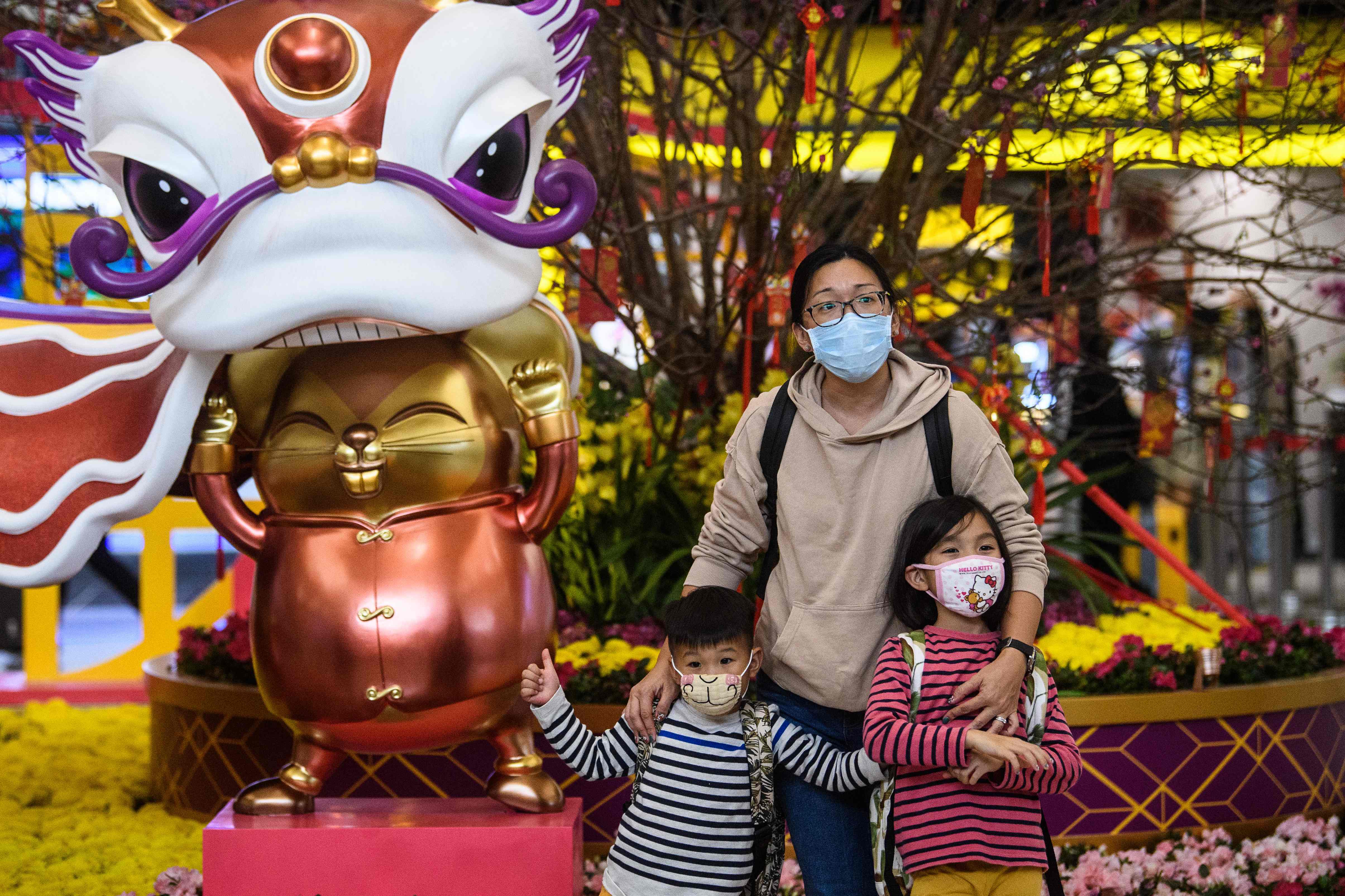 Ibu dan dua anaknya menggunakan masker saat berfoto di depan instalasi perayaan Tahun Baru Imlek di Hong Kong.
