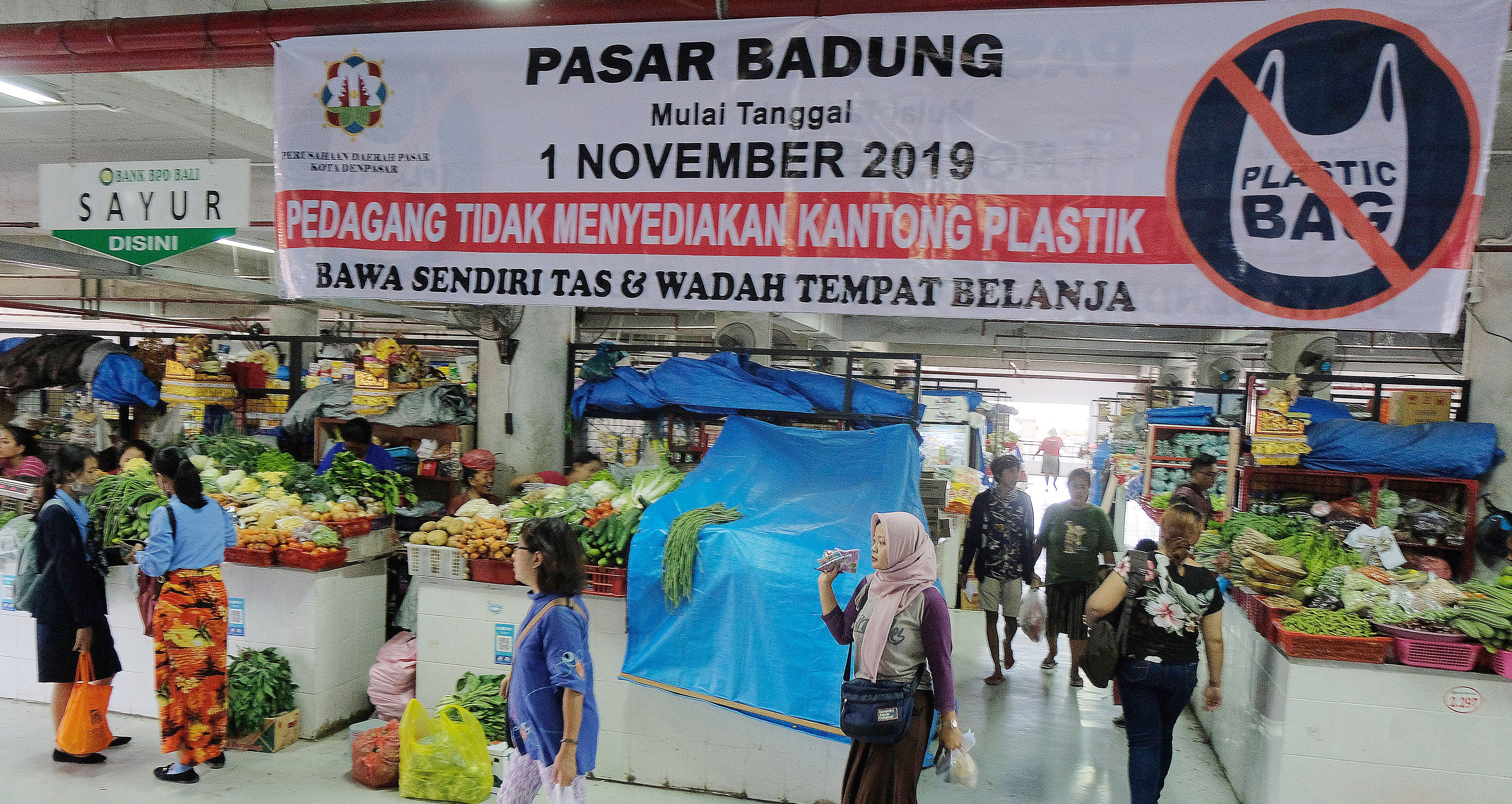 Ilustrasi: Pengunjung melintas di dekat spanduk pemberitahuan terkait pengurangan penggunaan kantong plastik belanja di Pasar Badung, Bali