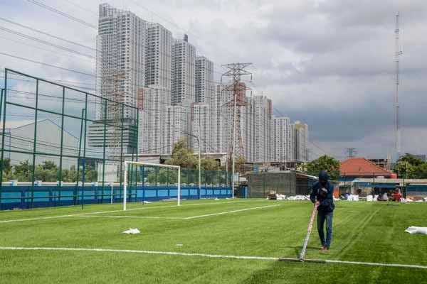 Pekerja melakukan perawatan rumput sintetis di lapangan sepakbola Muara Angke, Jakarta Utara.