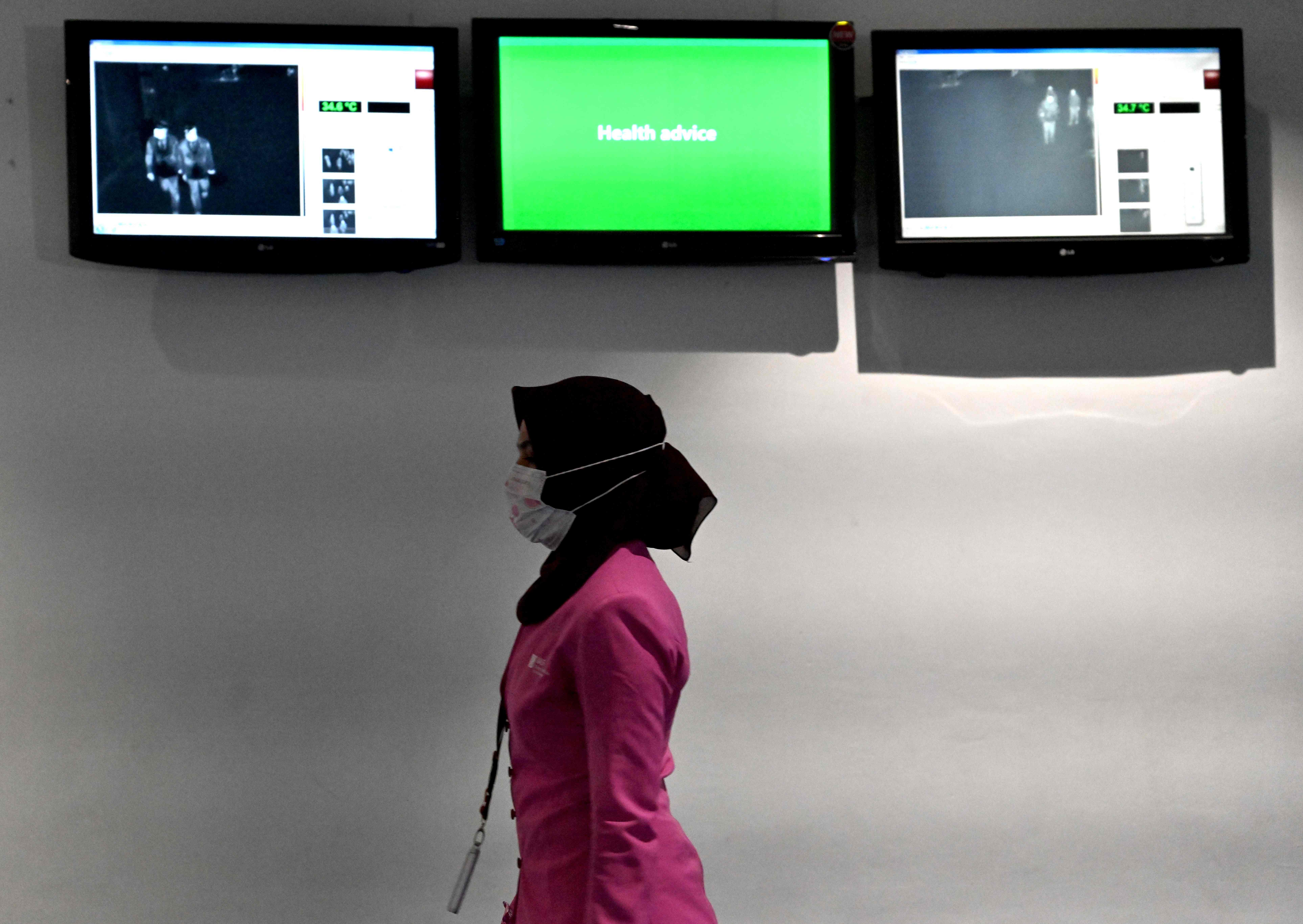 Seorang perempuan berjalan di bahwa monitor yang memperlihatkan gambar termal penumpang yang tiba di Bandara Soekarno-Hatta.
