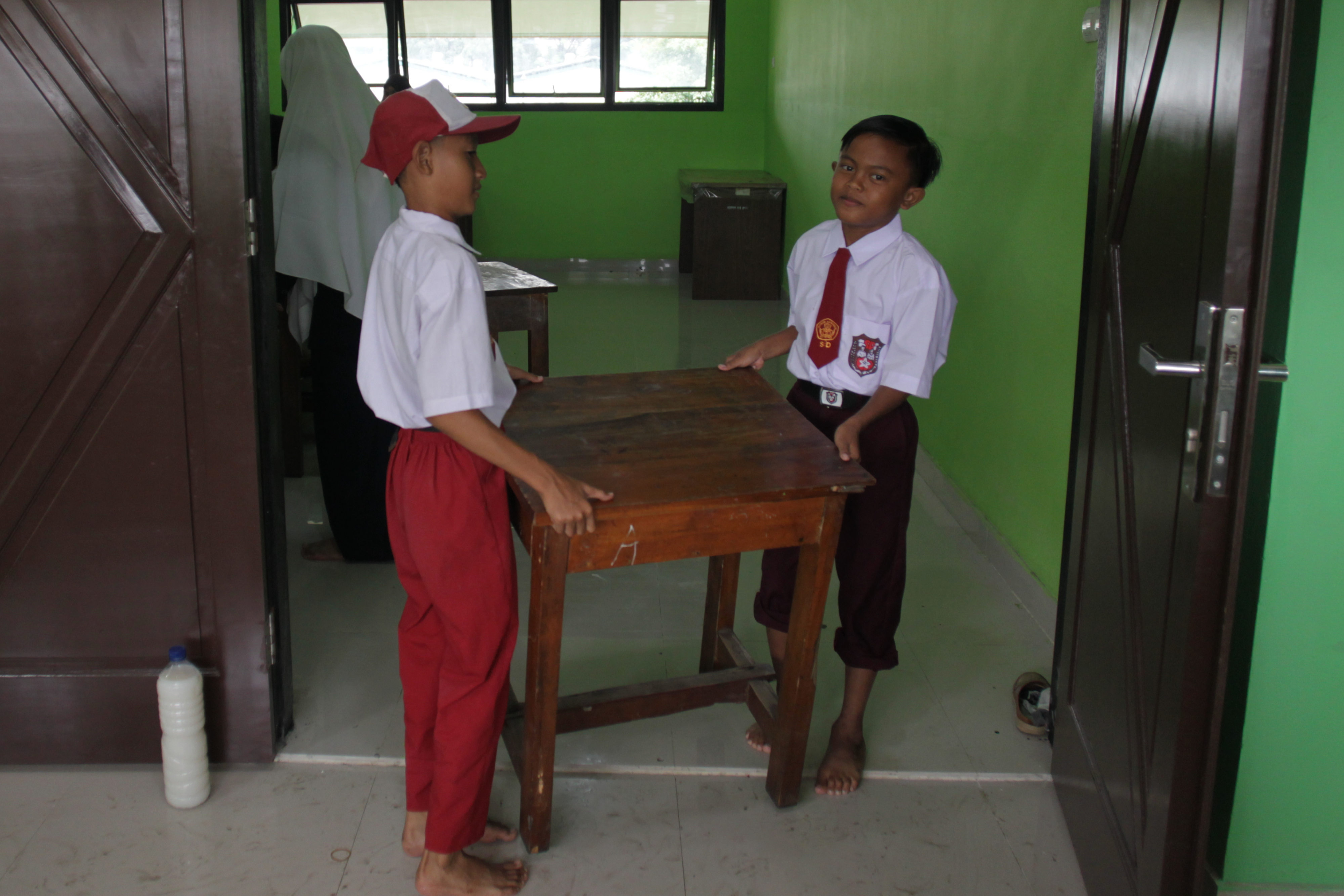 Siswa Sekolah Dasar Negeri Kapuk Muara 01 bergotong royong memindahkan meja, kursi, dan lemari kedalam ruang kelas saat kegiatan kerja bakti