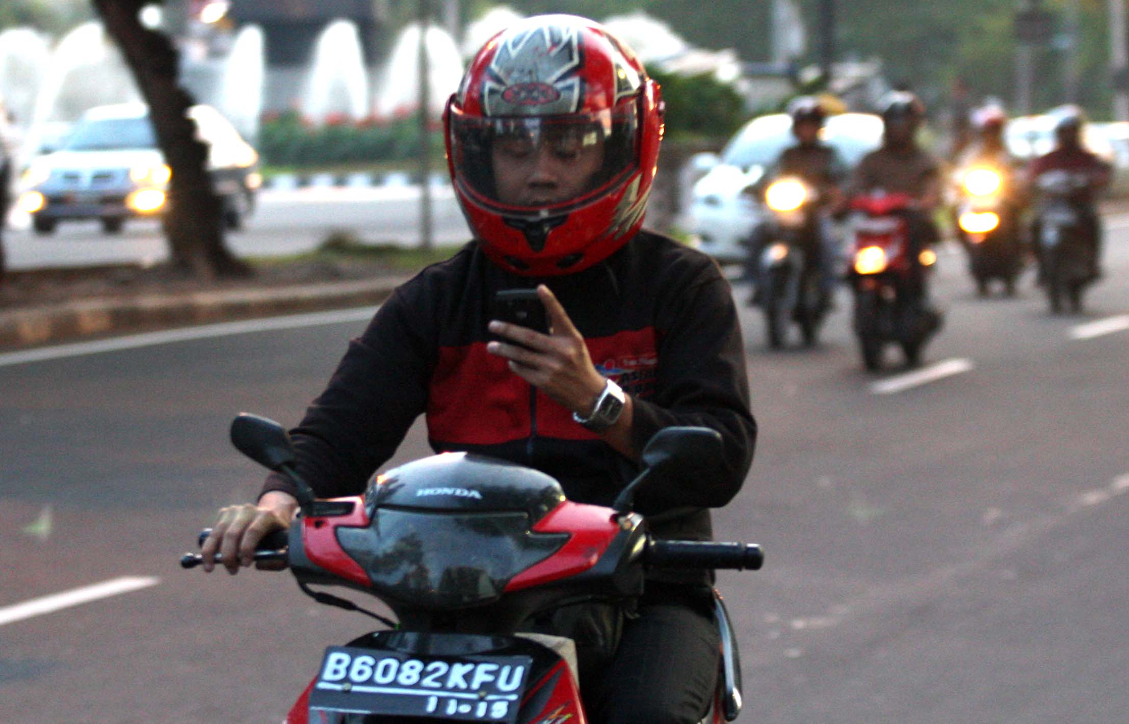 Ilustrasi pengendara motor menggunakan ponsel sambil berkendara