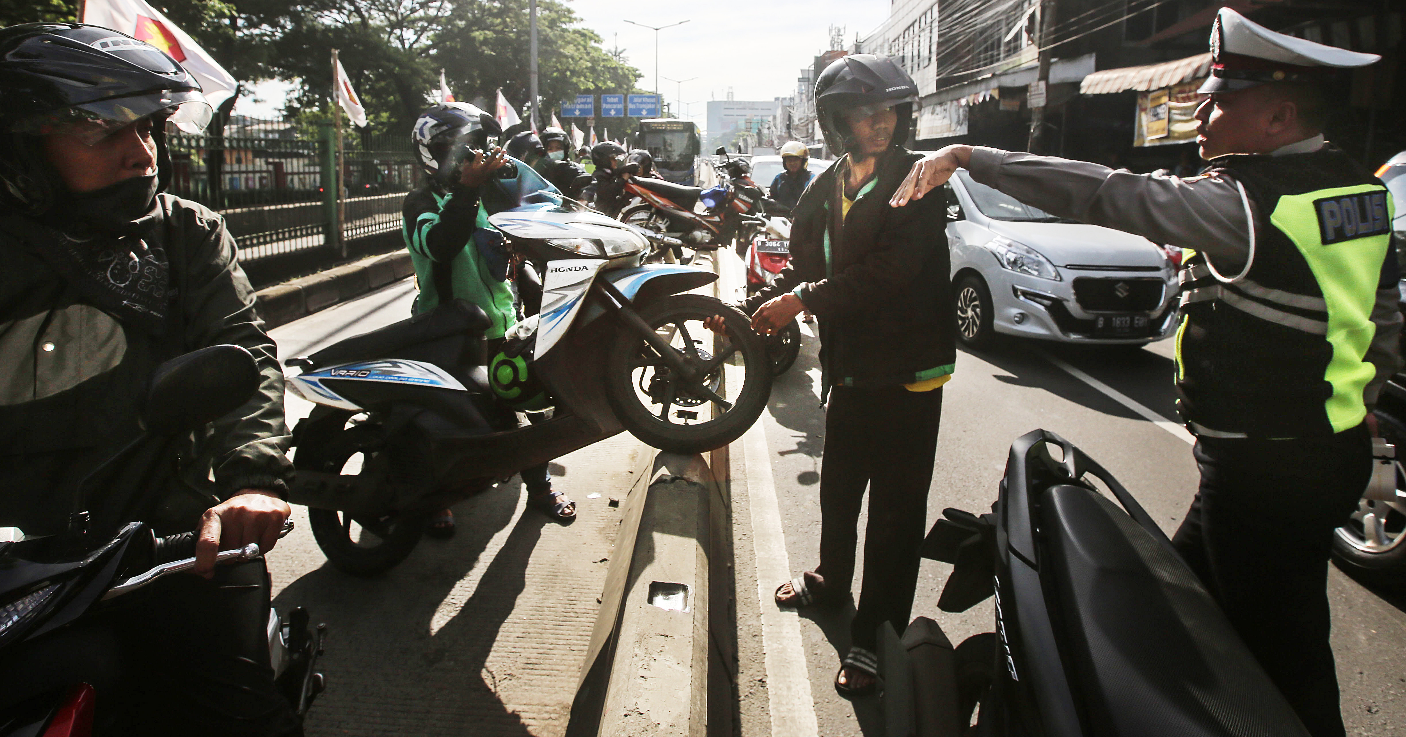 Polisi berusaha menghalangi pengendara sepeda motor yang saling bantu mengangkat motor melewati pembatas jalur Trans-Jakarta.