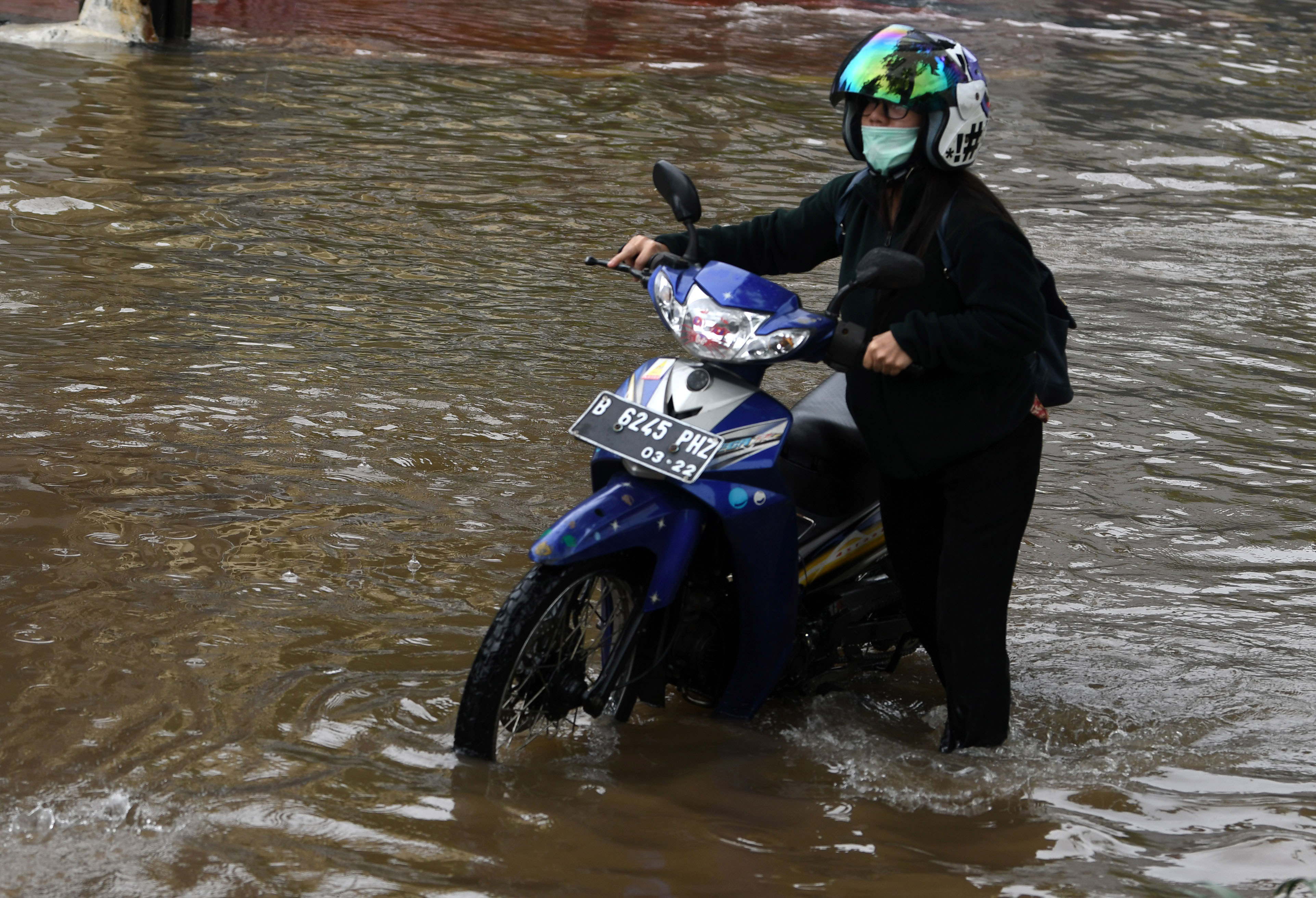 Warga menuntun sepeda motornya yang mogok karena melintasi banjir di Jalan Bungur Raya di Kemayoran, Jakarta.