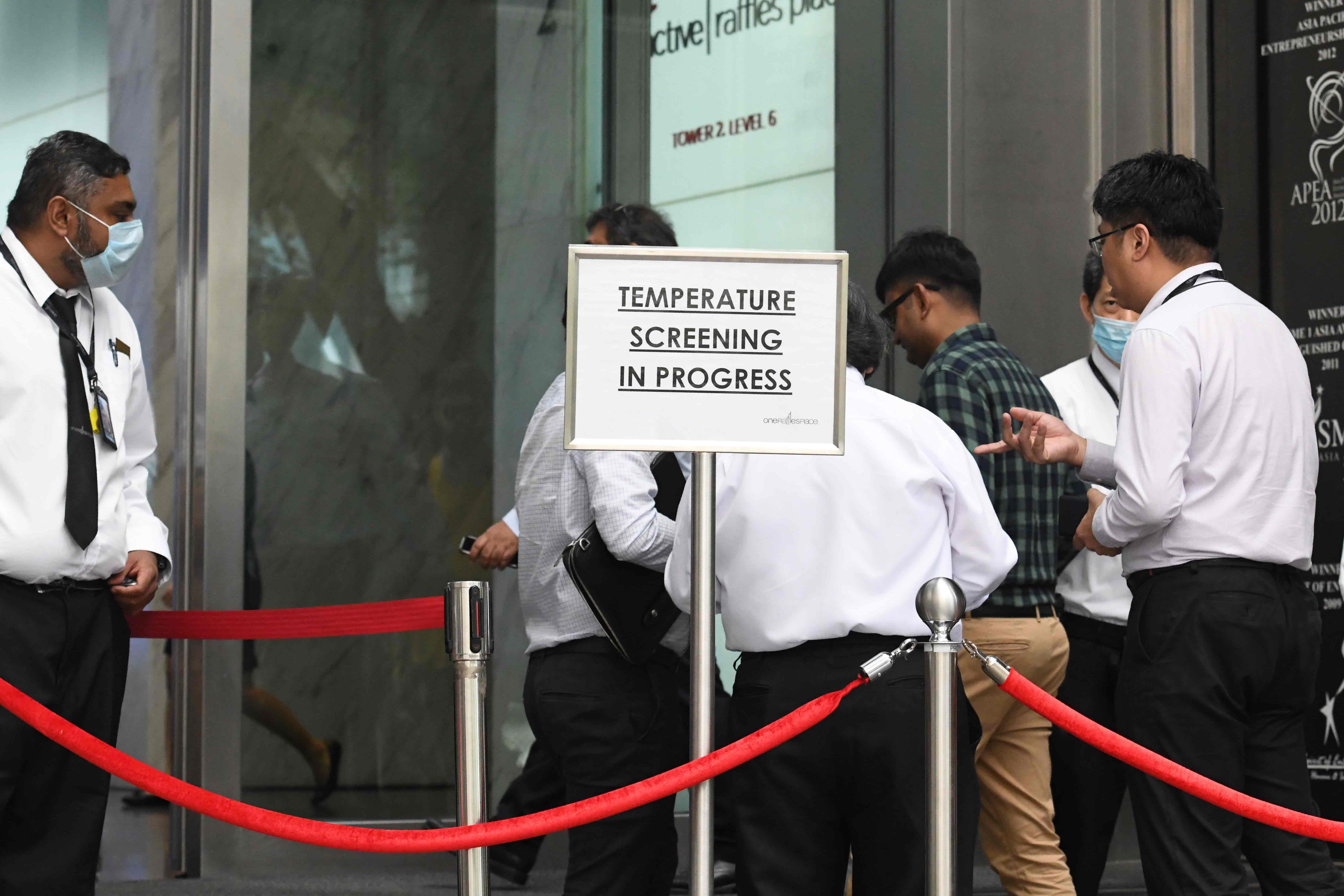 Prosedur pengecekan suhu tubuh di sebuah gedung perkantoran di pusat bisnis Singapura