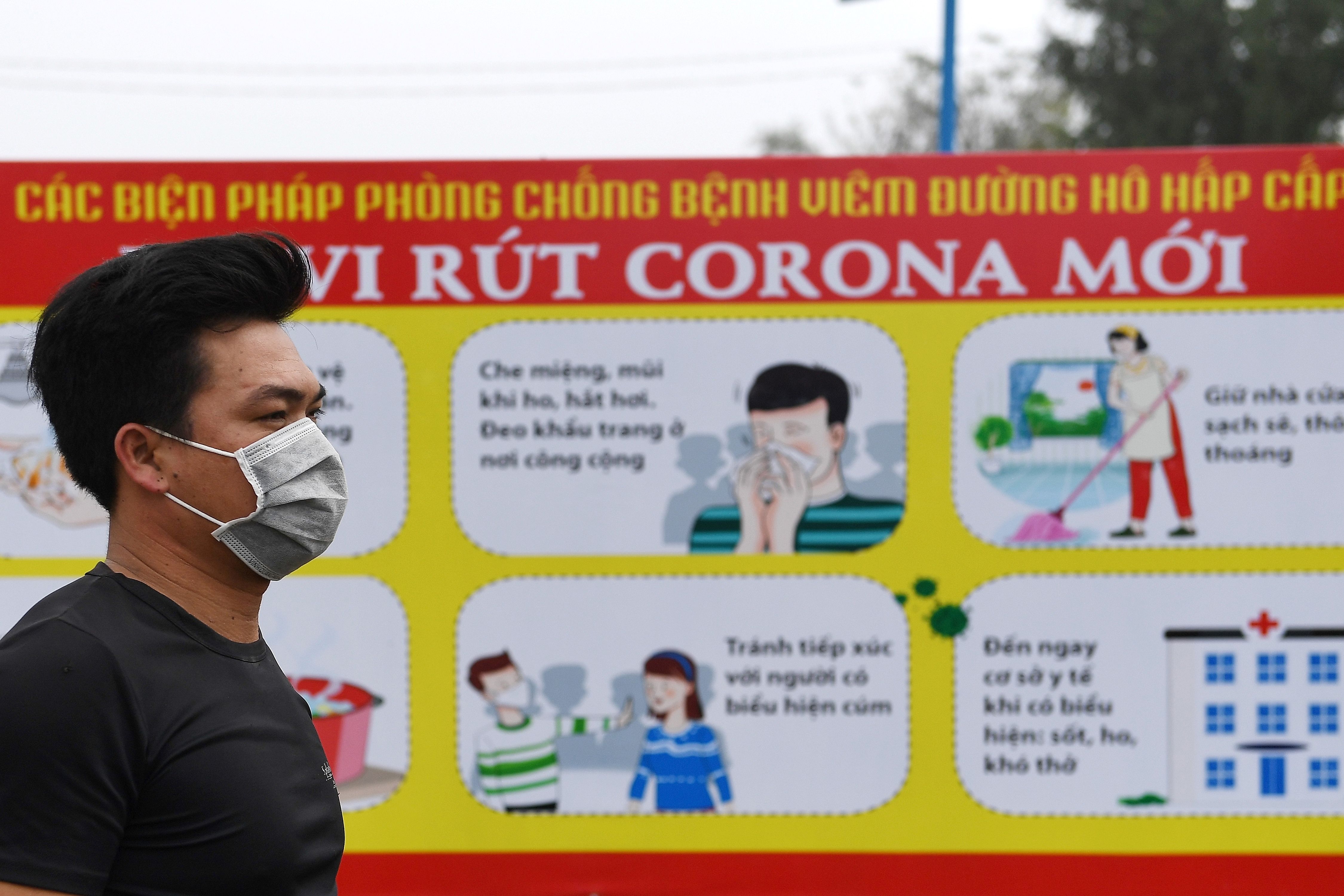 Seorang pria mengenakan masker melintas di depan spanduk yang menampilkan cara menghindar dari virus korona di Son Loi, Vietnam.