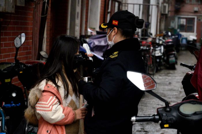 Seorang petugas keamanan memeriksa suhu tubuh seorang warga di komplek perumahan di Shanghai, Tiongkok.