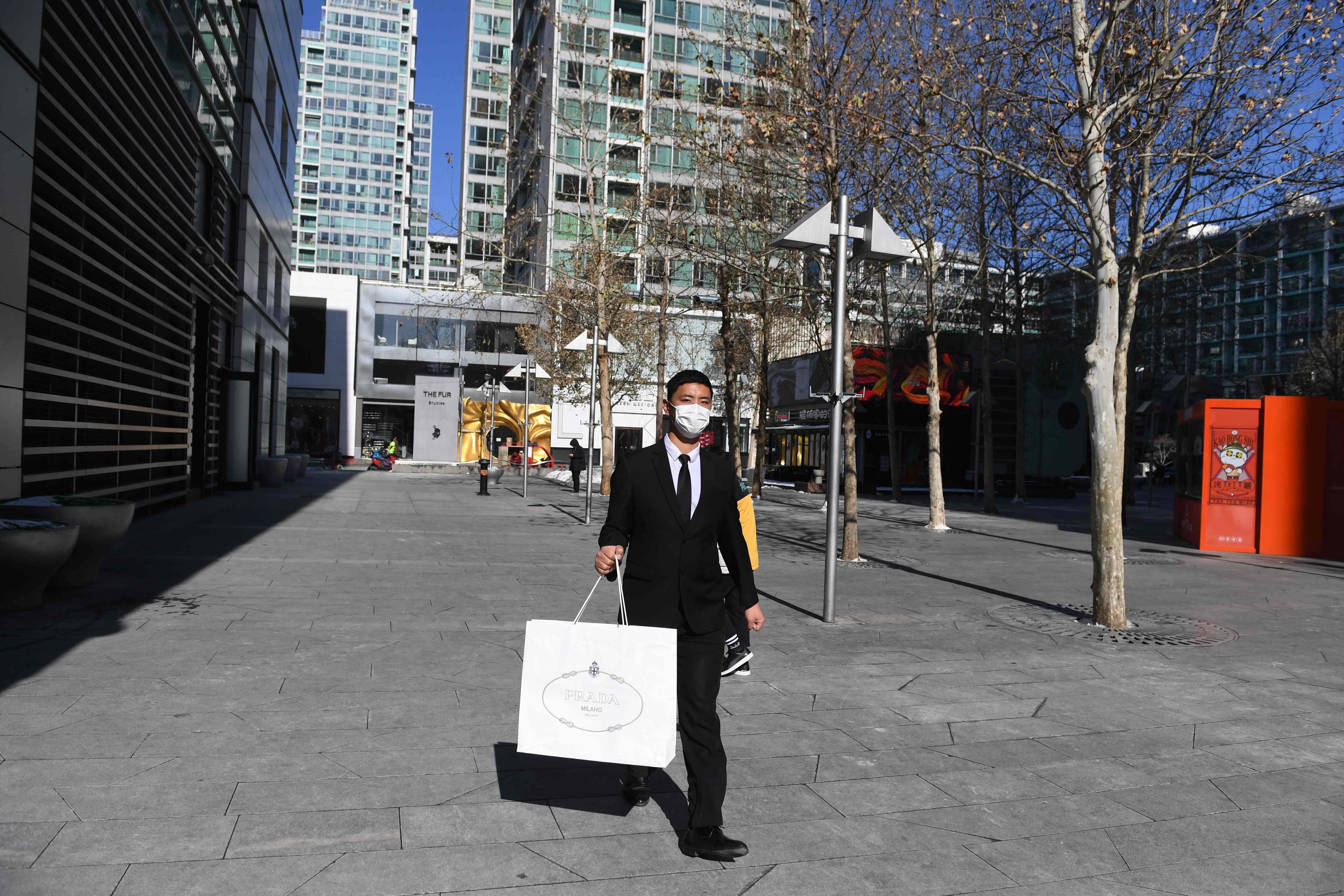 Seorang pria berjalan membawa tas belanja di luar mal mewah yang hampir sepi di Beijing, kemarin.