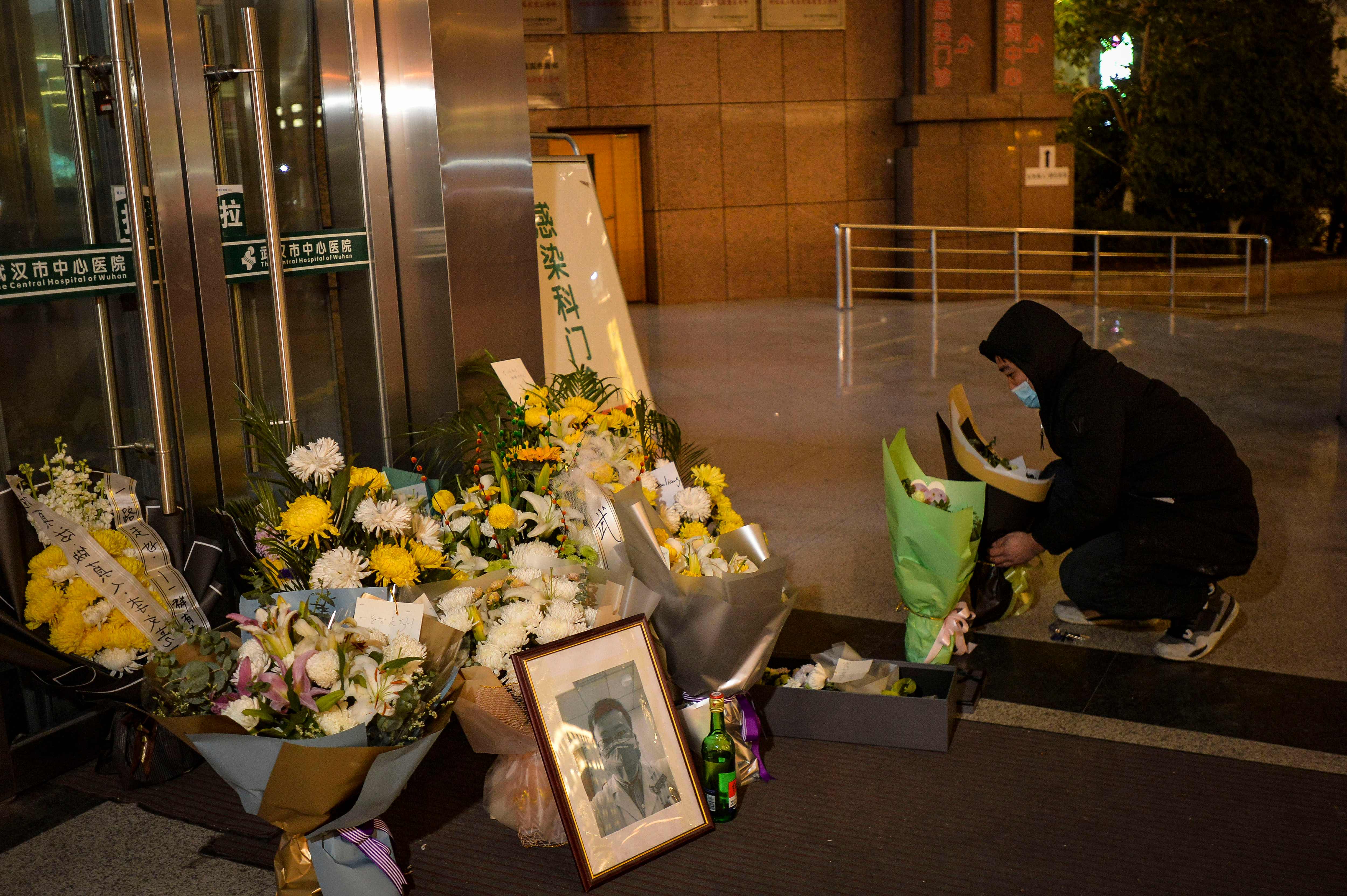 Seorang pria mengenakan masker meletakkan bunga di dekat foto dokter Li Wenliang. Li adalah dokter yang pertama melaporkan virus korona.