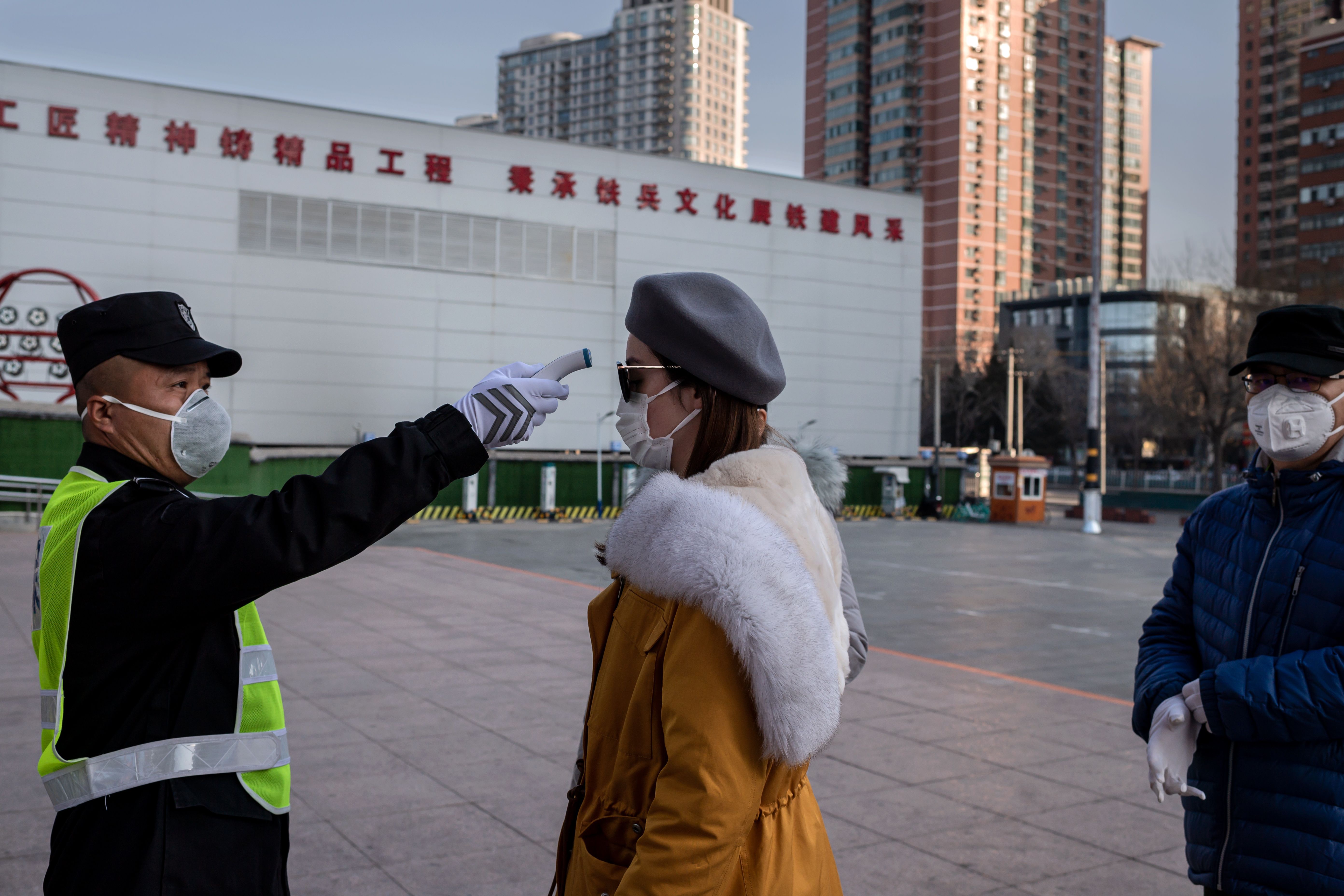 Seorang petugas memeriksa suhu tubuh seorang perempuan sebelum memasuki sebuah taman di Beijing, Tiongkok