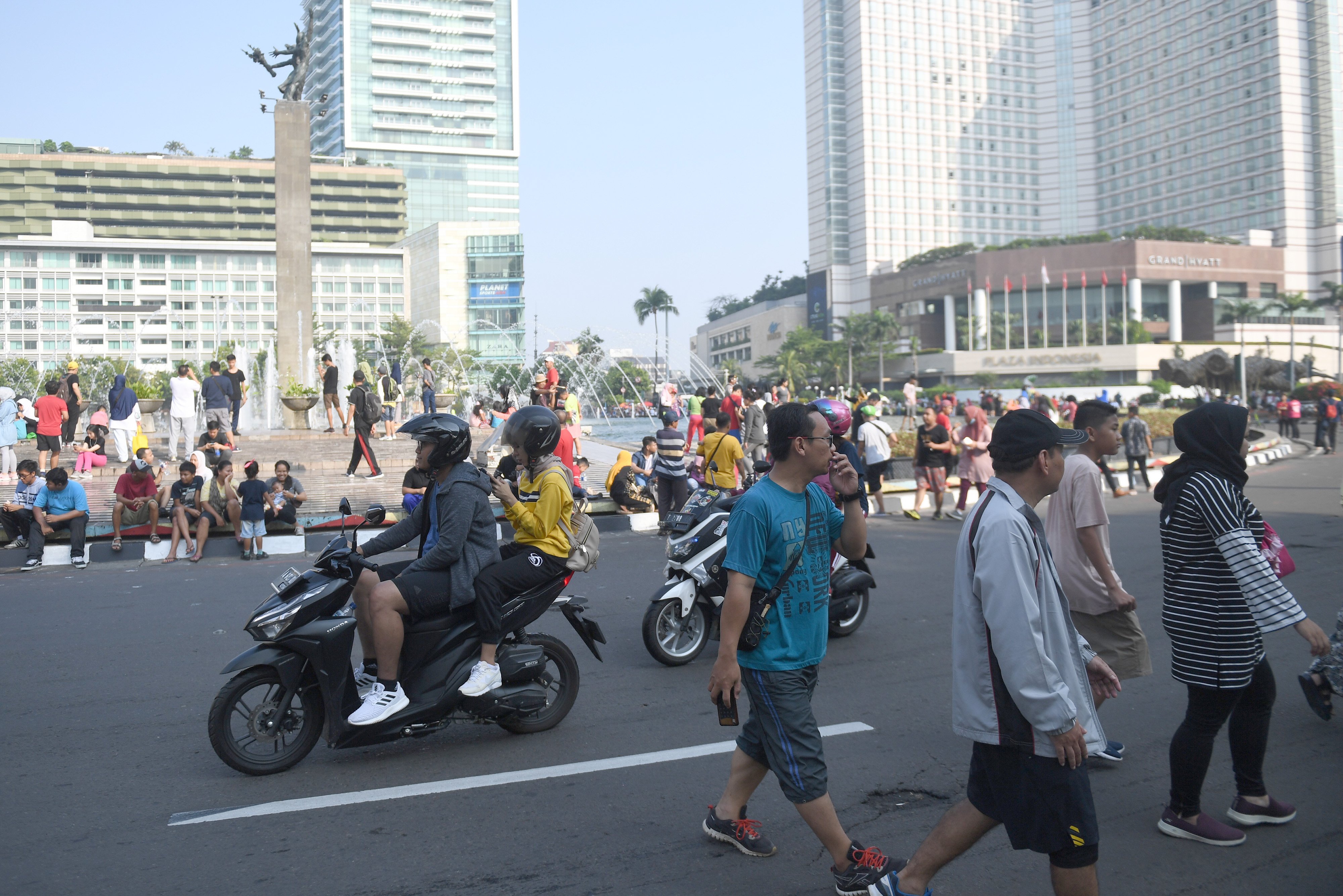 Warga beraktifitas di antara kendaraan yang melaju di Bundaran HI, Jakarta.