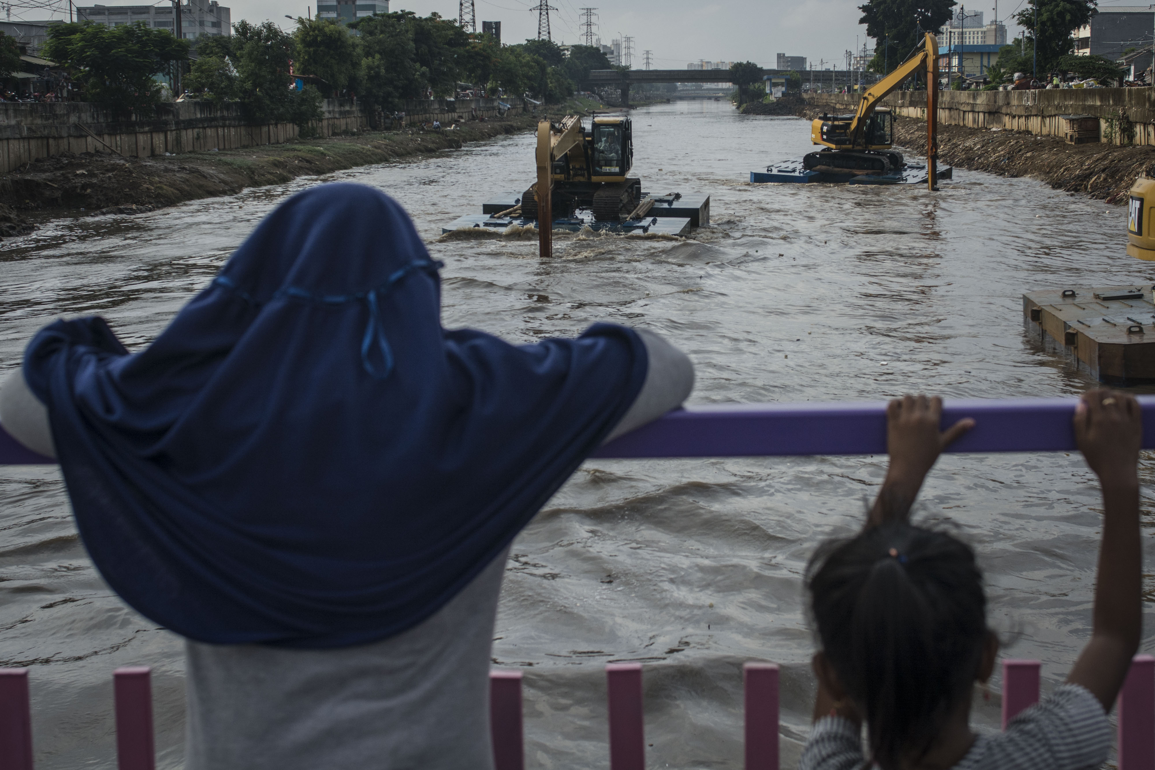 Warga menyaksikan alat berat mengeruk endapan lumpur sungai Ciliwung, di Kanal Banjir Barat (KBB), Tanah Abang