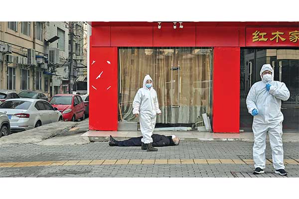 Dua petugas medis berada di dekat pria yang jatuh pingsan dan meninggal di Kota Wuhan, Tiongkok, Kamis (30/1).